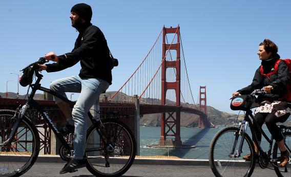 Tourists ride bicycles past the Golden Gate Bridge.