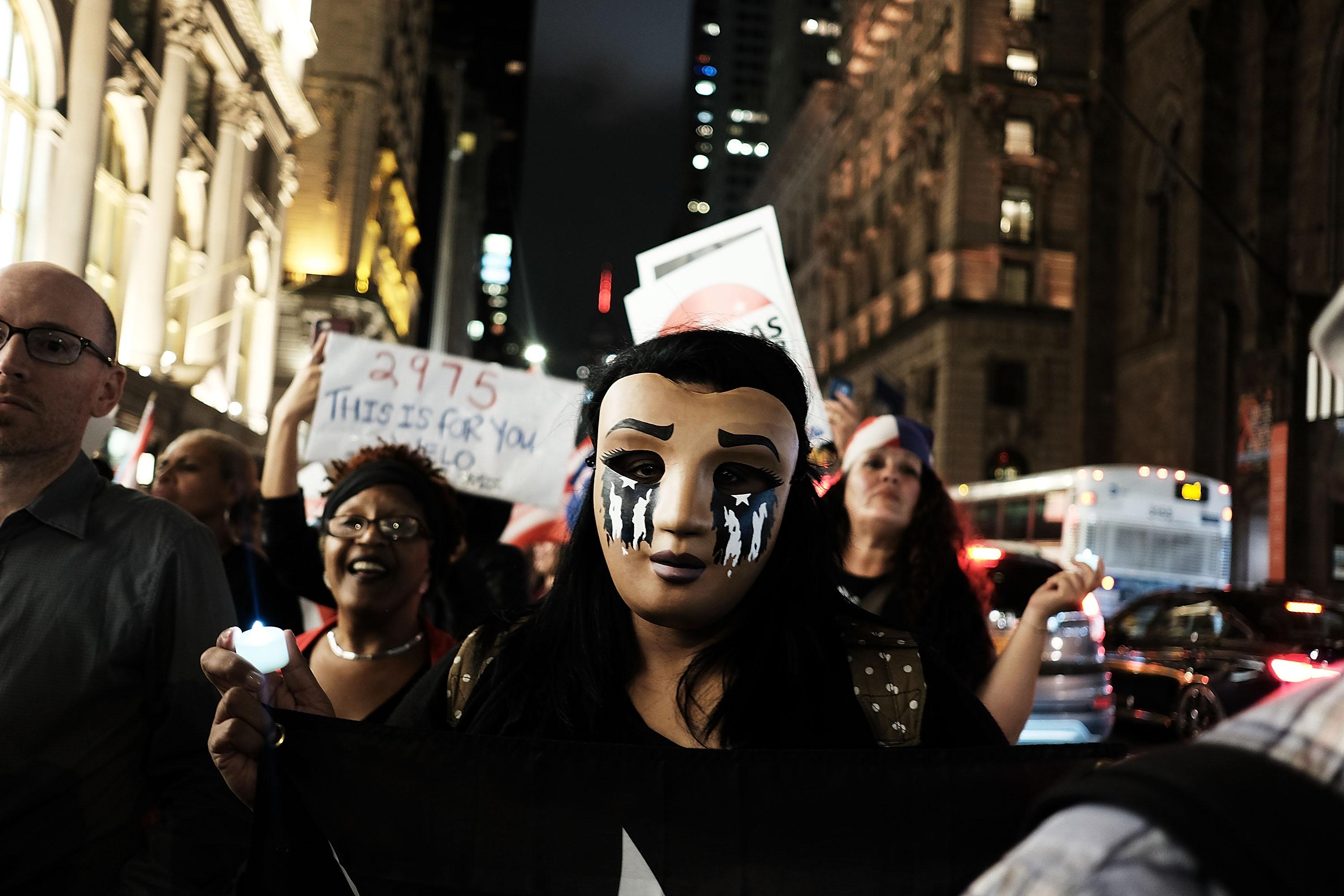 A person wearing a mask decorating to look like it is weeping leads a march in New York.