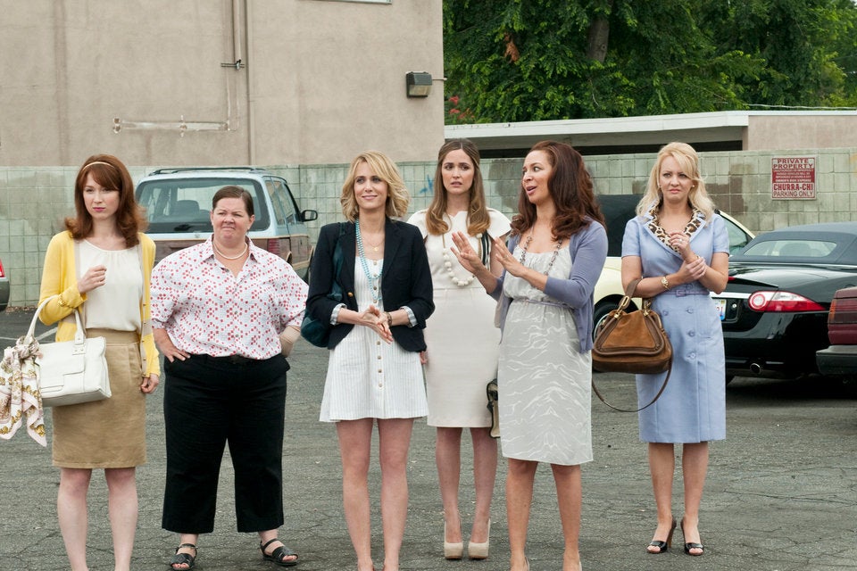 A group of women stands in pastel colors in a parking lot. From left to right, Ellie Kemper, Melissa McCarthy, Kristen Wiig, Rose Byrne, Maya Rudolph, and Wendi McLendon-Covey