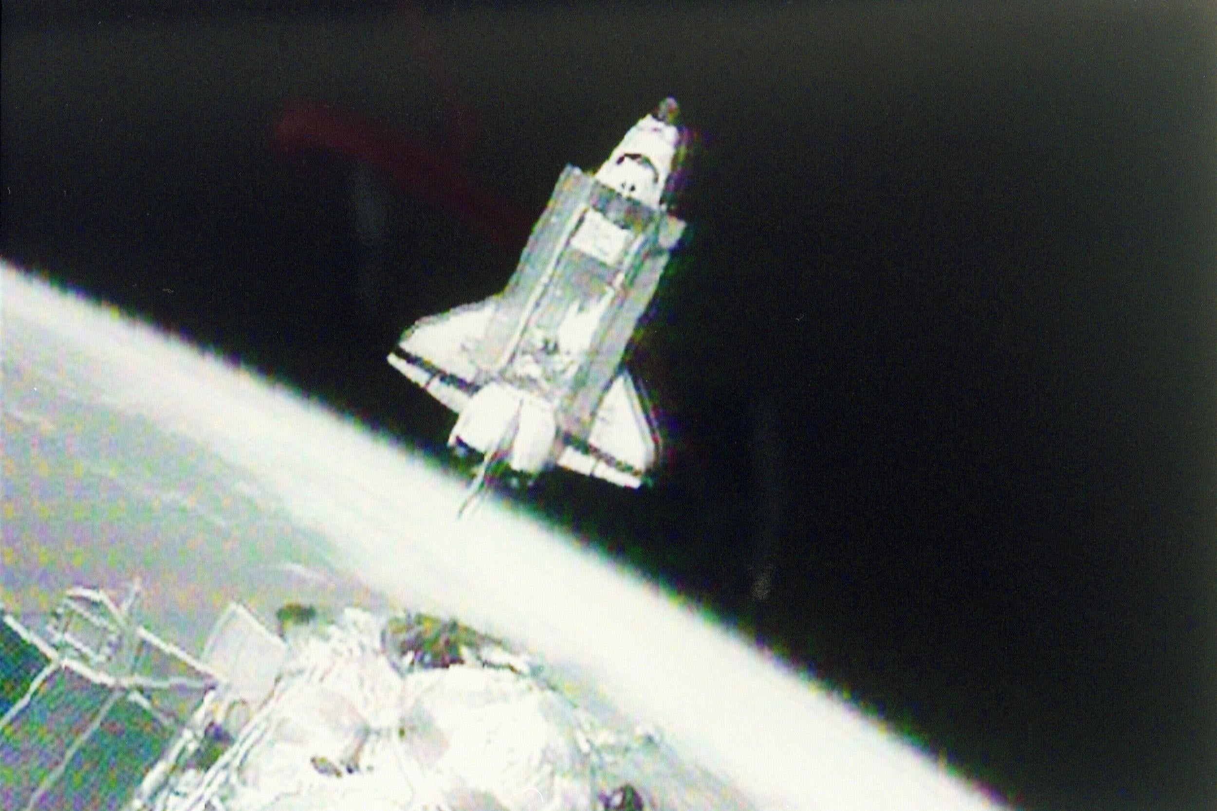 A grainy image of the space shuttle, its bay doors open, and Earth visible below.