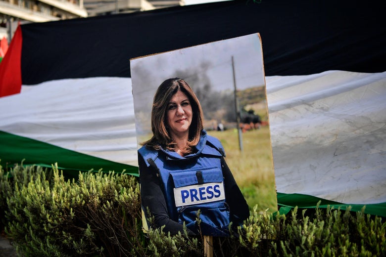 A photo of Shireen Abu Akleh is seen on top of grass and in front of a flag.