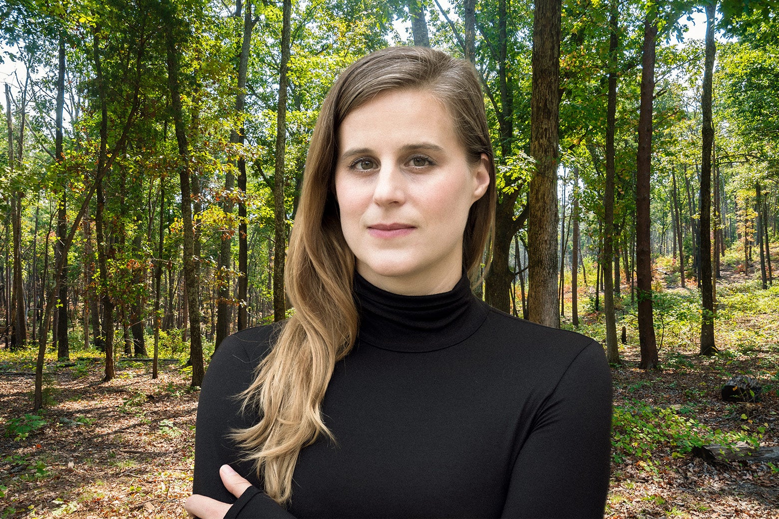 A woman in a black turtleneck looks at the camera. Behind her, a sunlit forest.