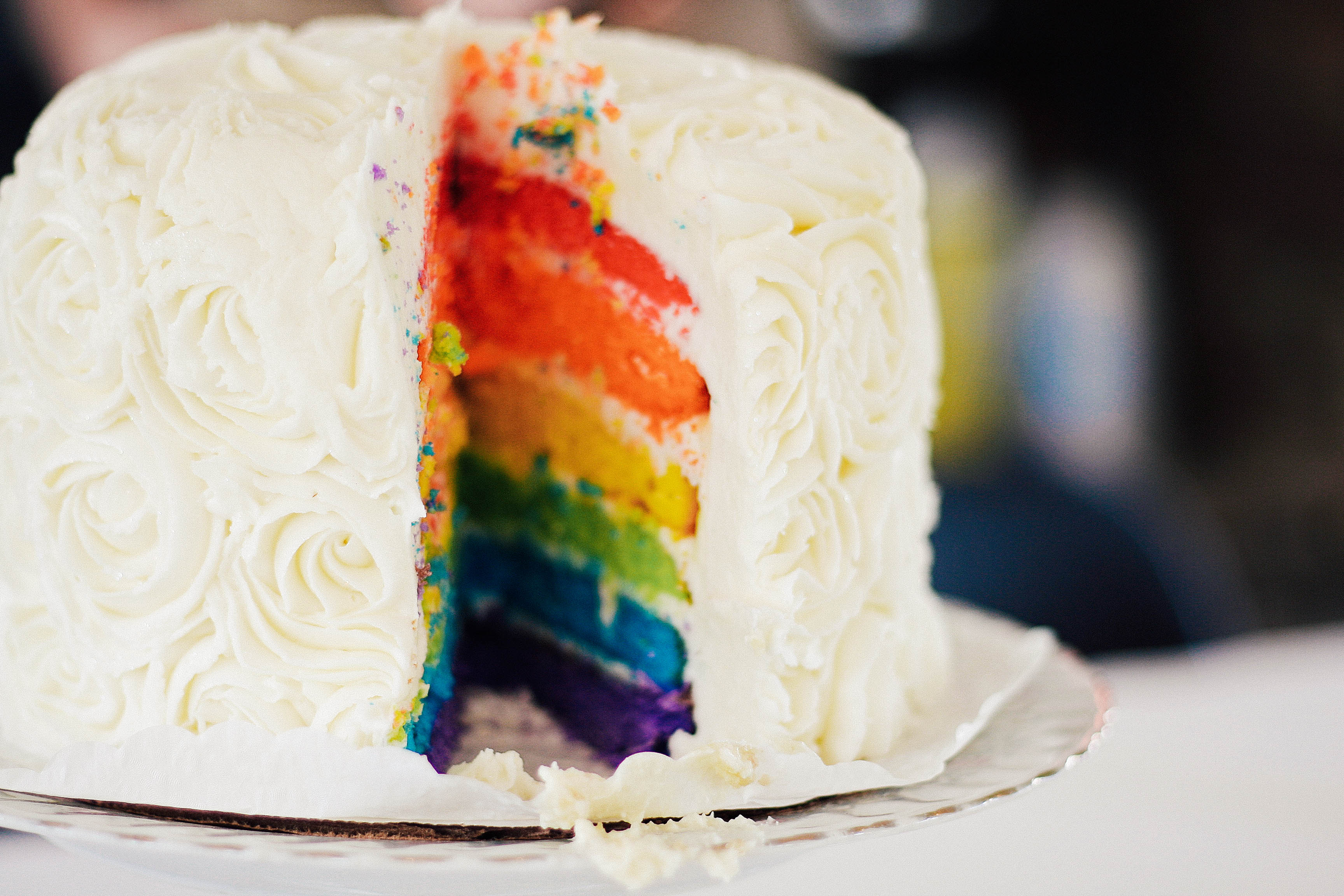 A rainbow cake that has had a slice cut out of it, revealing the colorful layers