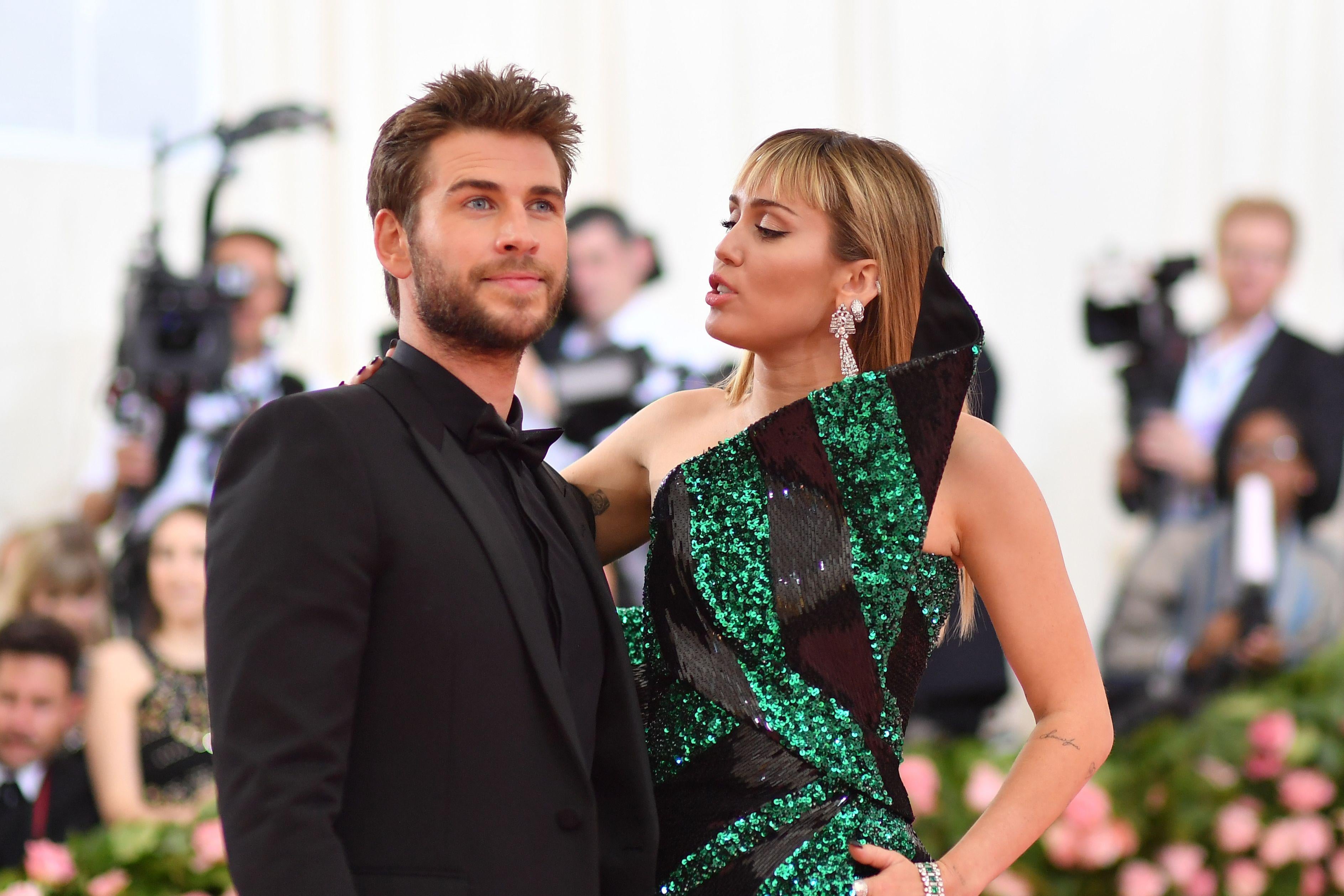 Miley Cyrus (R) and Liam Hemsworth stand on the red carpet at the 2019 Met Gala.