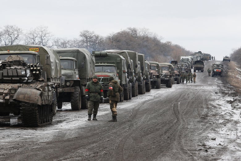 A military convoy drives down a gravel road with light snow cover.