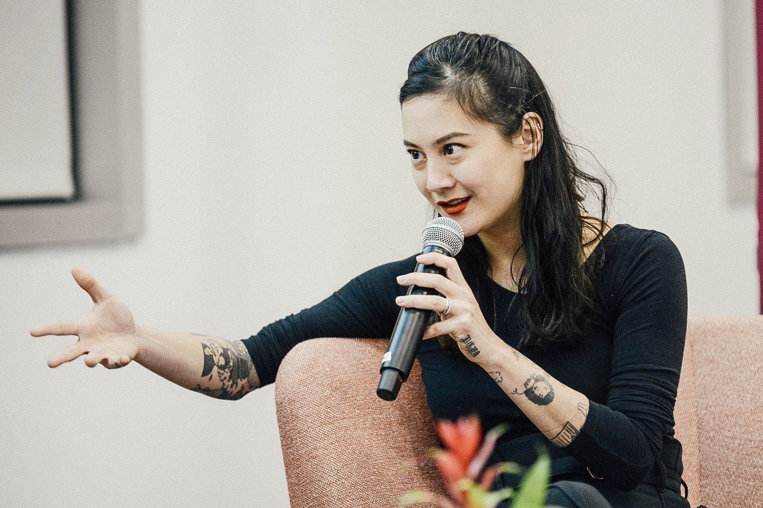 Zauner seated at an event. She is speaking into a mic she holds in one hand as she gestures with the other hand.
