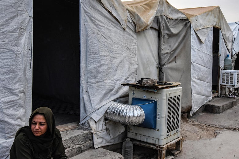 A woman sits outside a tent with an air-conditioning unit.