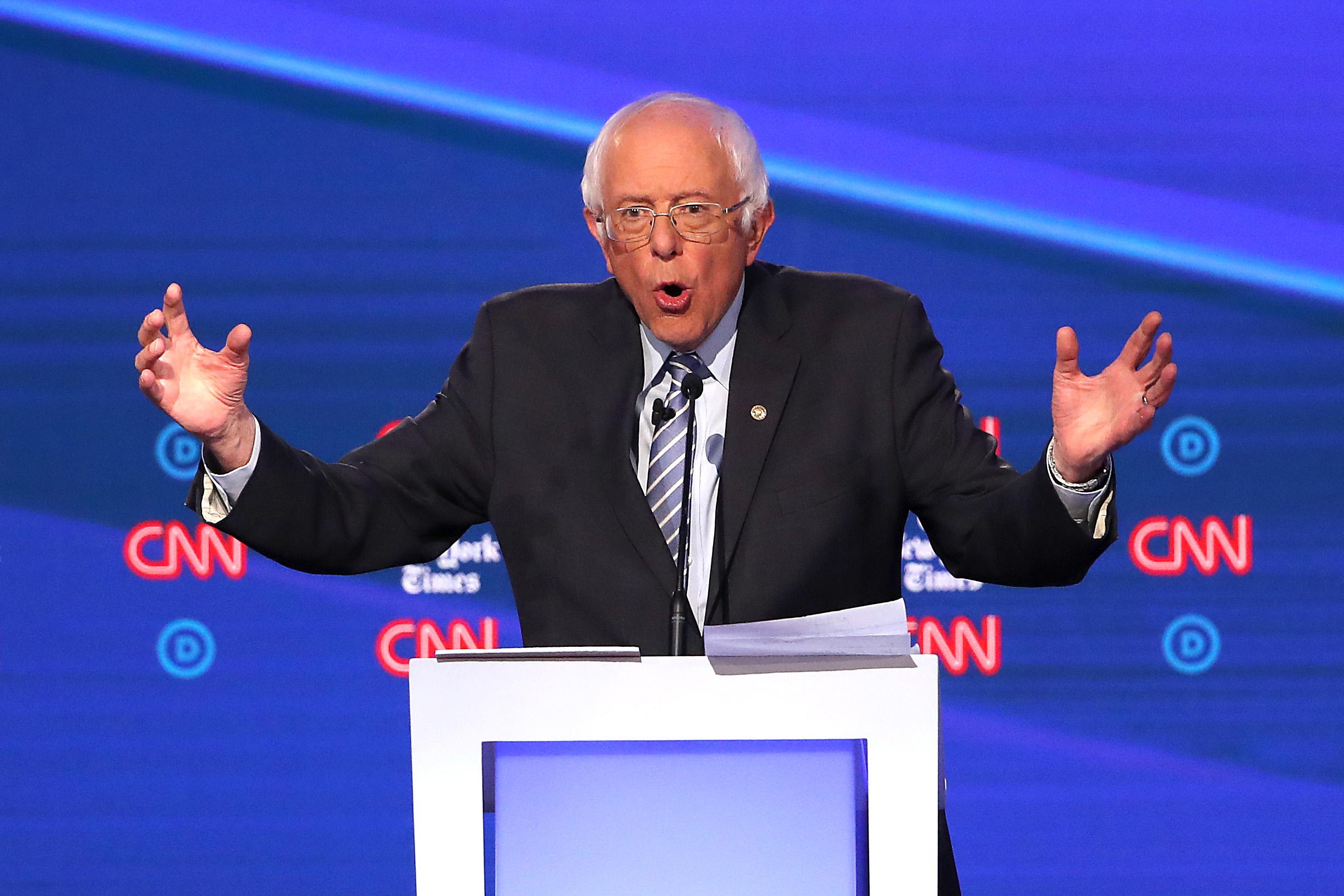 Bernie Sanders, midsentence, holds his arms out on the debate stage