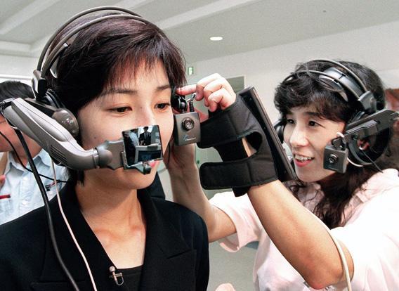 A woman helps another put American computer venture company Xybernaut's wearable PC 'Mobile Assistant IV' on her head.