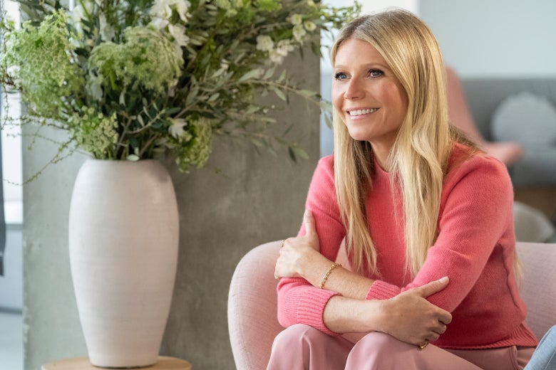 Gwyneth  Paltrow sits and smiles while wearing a salmon-colored shirt.