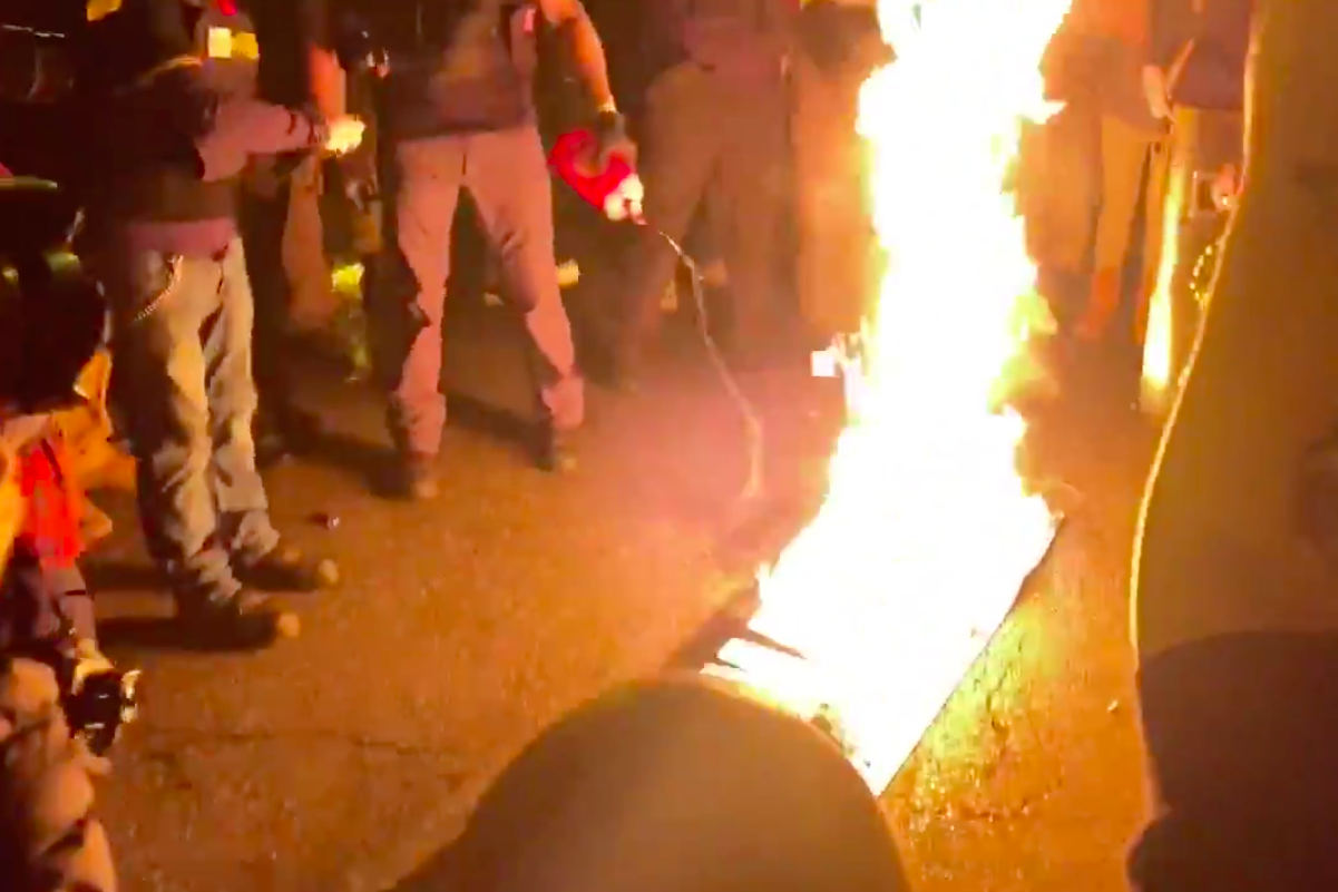 Screenshot of a video of a crowd surrounding a Black Lives Matter flag burning on the ground at night
