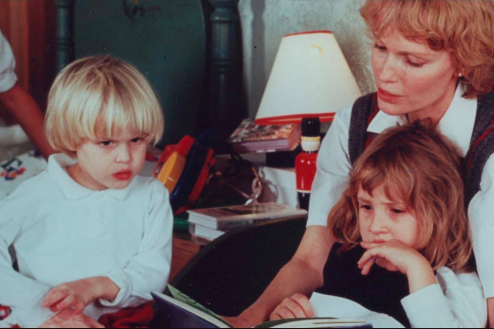 All three have long hair—Ronan’s blonde hair is in a long bowl cut—as Mia appears to read to them from a children’s book