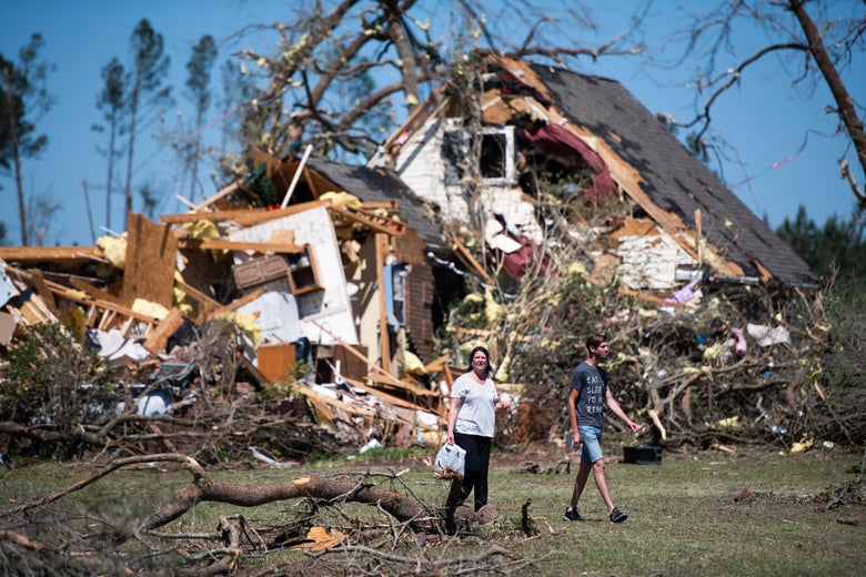 Two women walk in front of a destroyed house and felled trees
