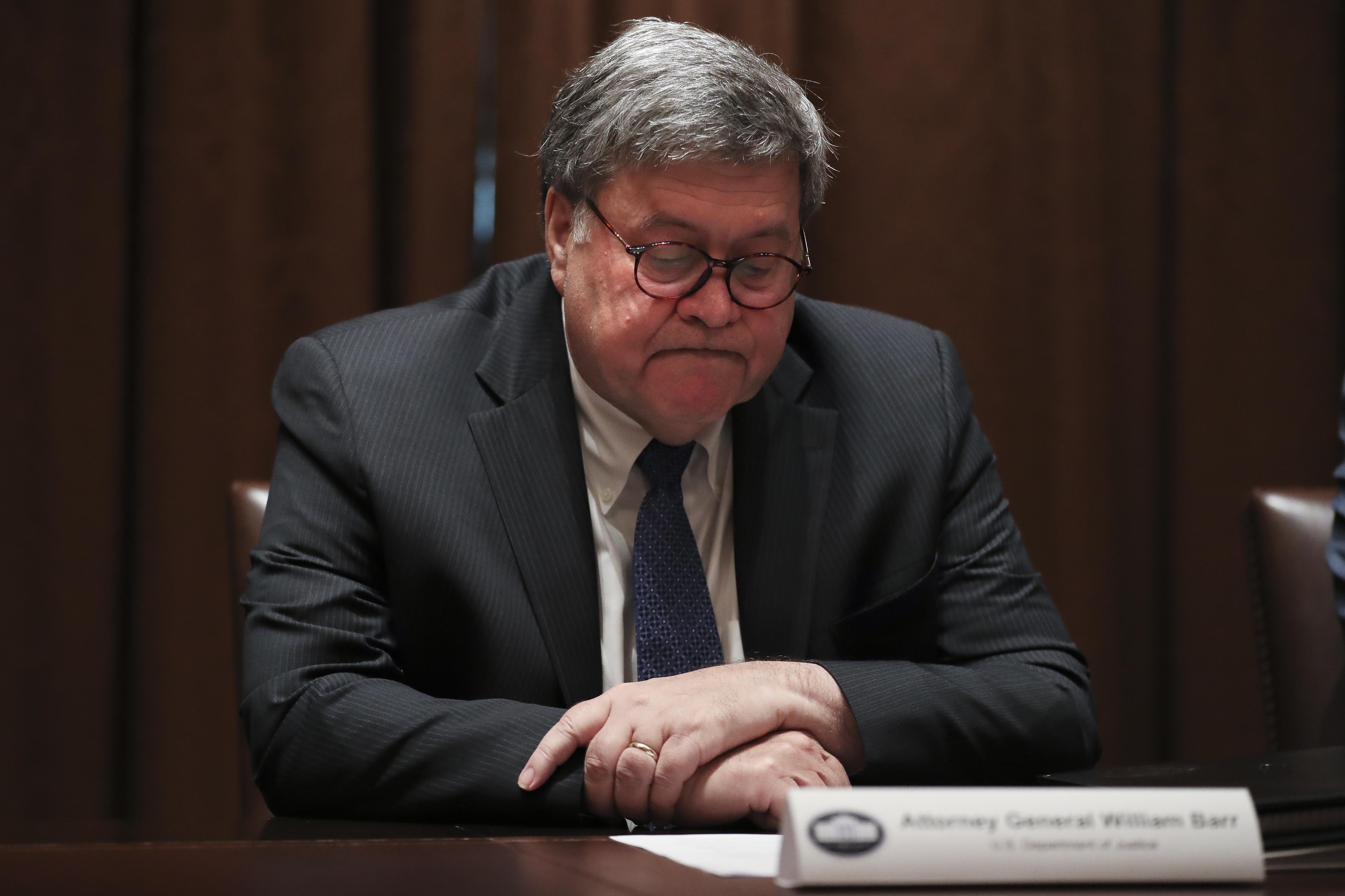 Attorney General William Barr looks down at a notepad while sitting at a table at the White House.
