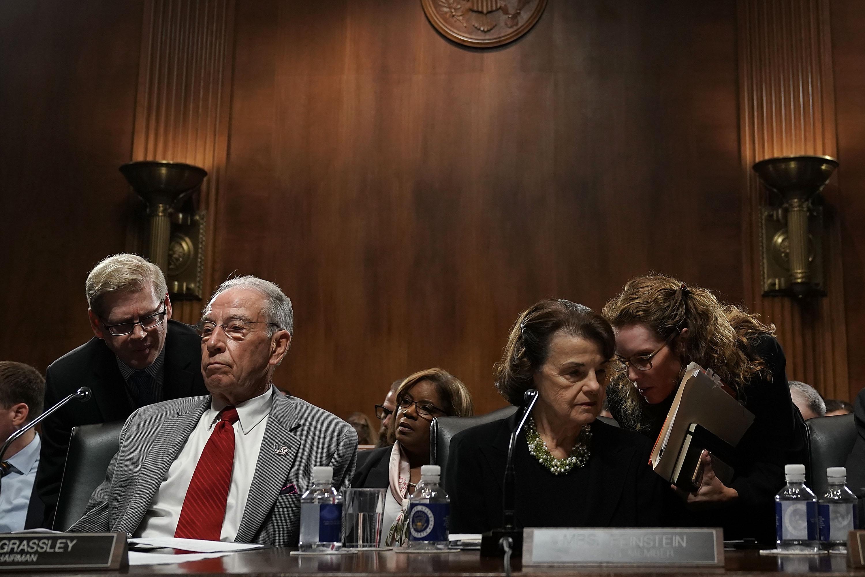 Aides lean in to talk to Sens. Chuck Grassley and Dianne Feinstein during a hearing.