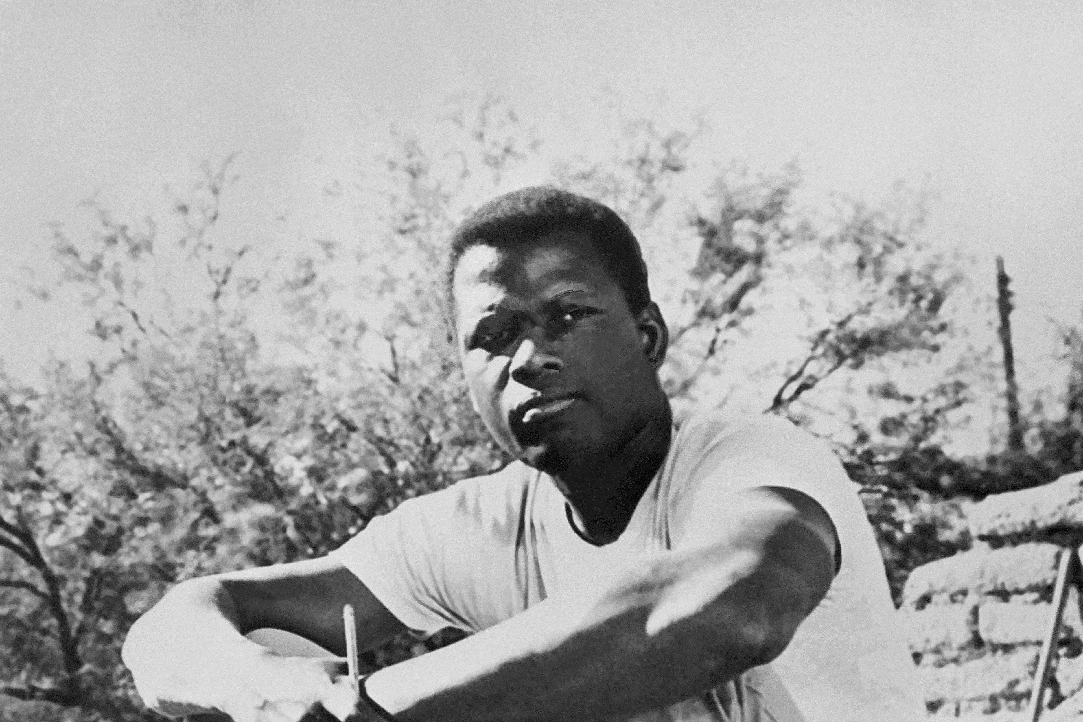 Sidney Poitier sits, arms on knees, looking contemplative.