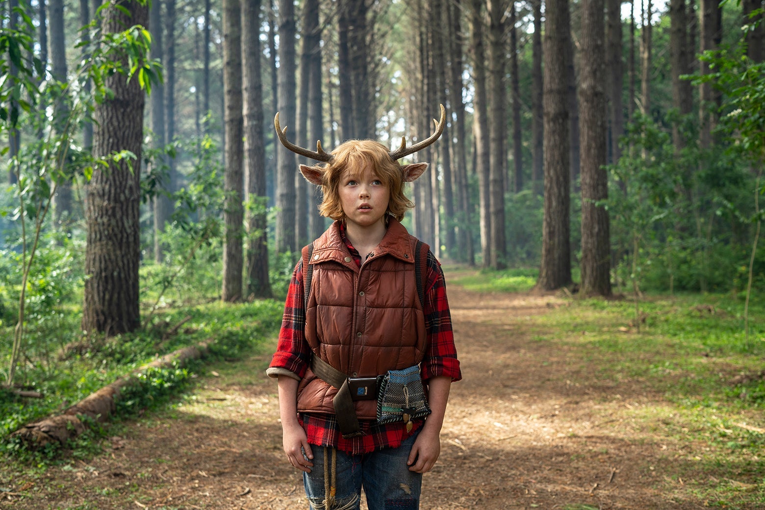 Actor Christian Convery as Gus, a boy with antlers on his head, standing in the woods in a still from Sweet Tooth.