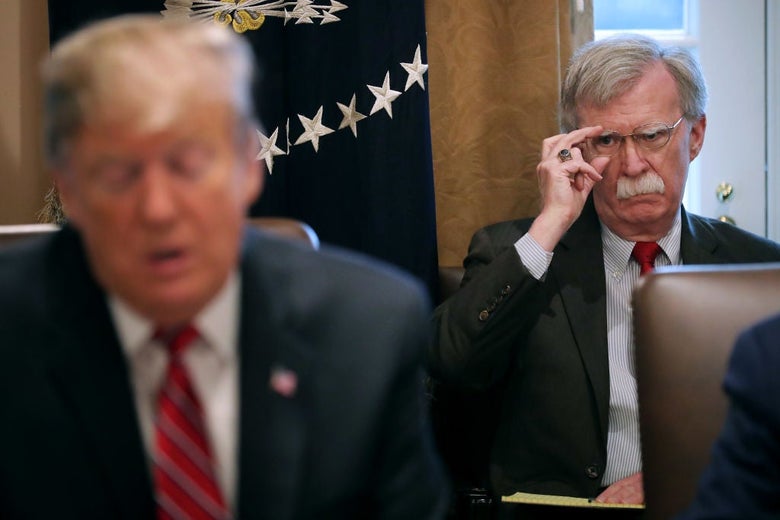 Bolton, seated behind Trump, frowns in his direction.