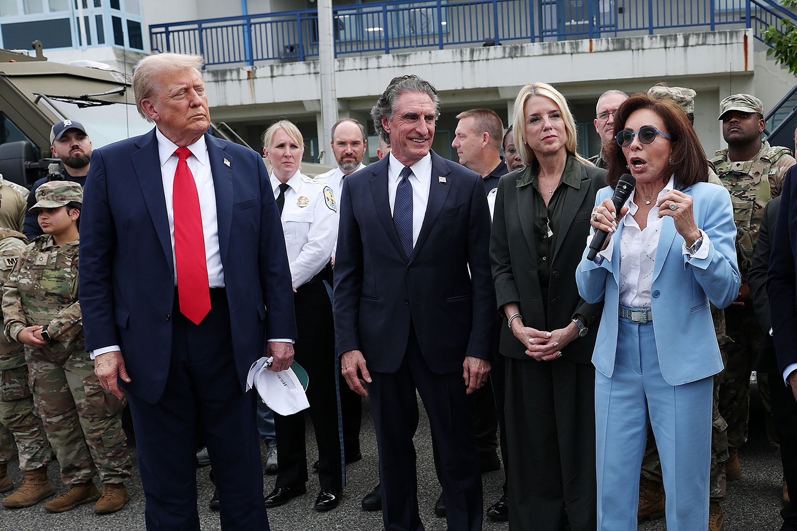 Burnam sorri largamente enquanto Pirro fala, Trump fecha os olhos e franze a testa, há tropas camufladas atrás deles.