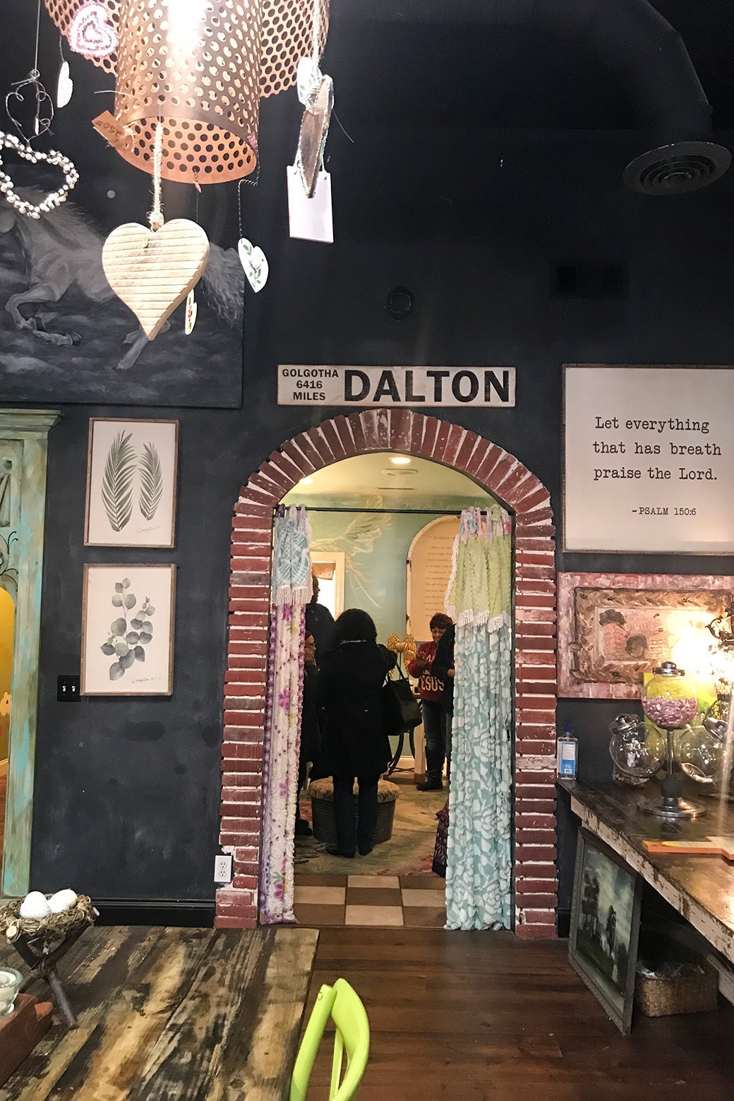 A small brick archway, on top of which is a sign for the city of Dalton. Surrounding the archway are various pictures, tables, a Bible verse, and some lights with hearts.
