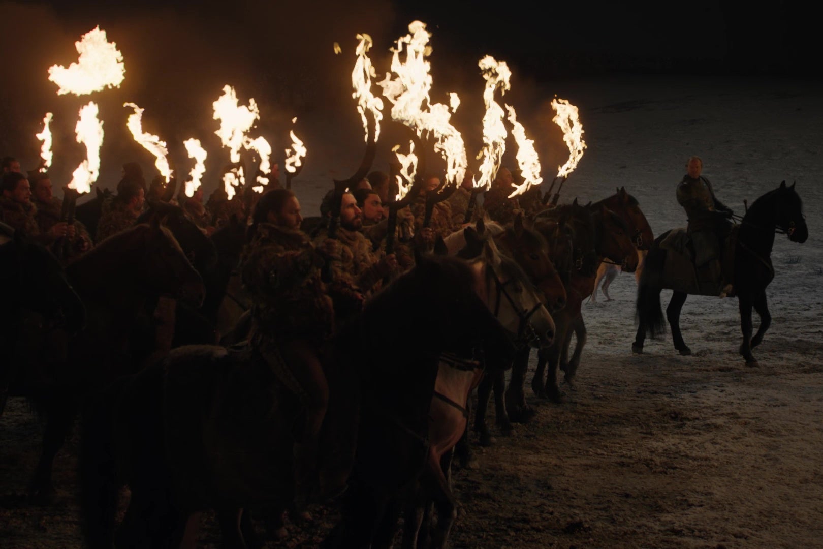 A group of Dothraki warriors on horseback hold up their flaming swords.