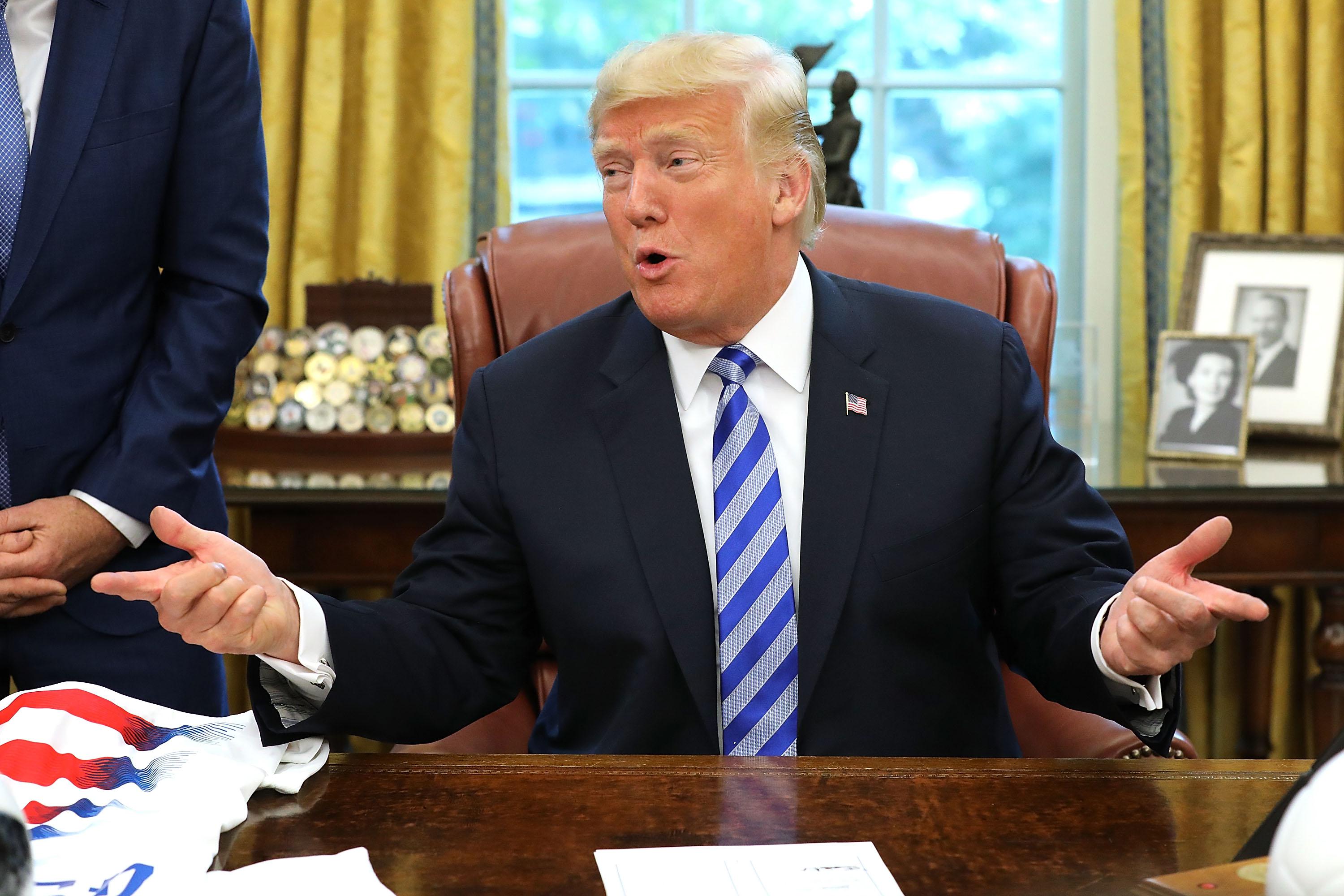 Donald Trump holds his arms out in the Oval Office