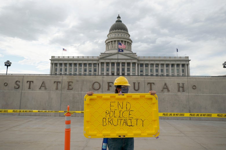 A person in a yellow helmet holds up a sign that says "End Police Brutality" outside the Capitol