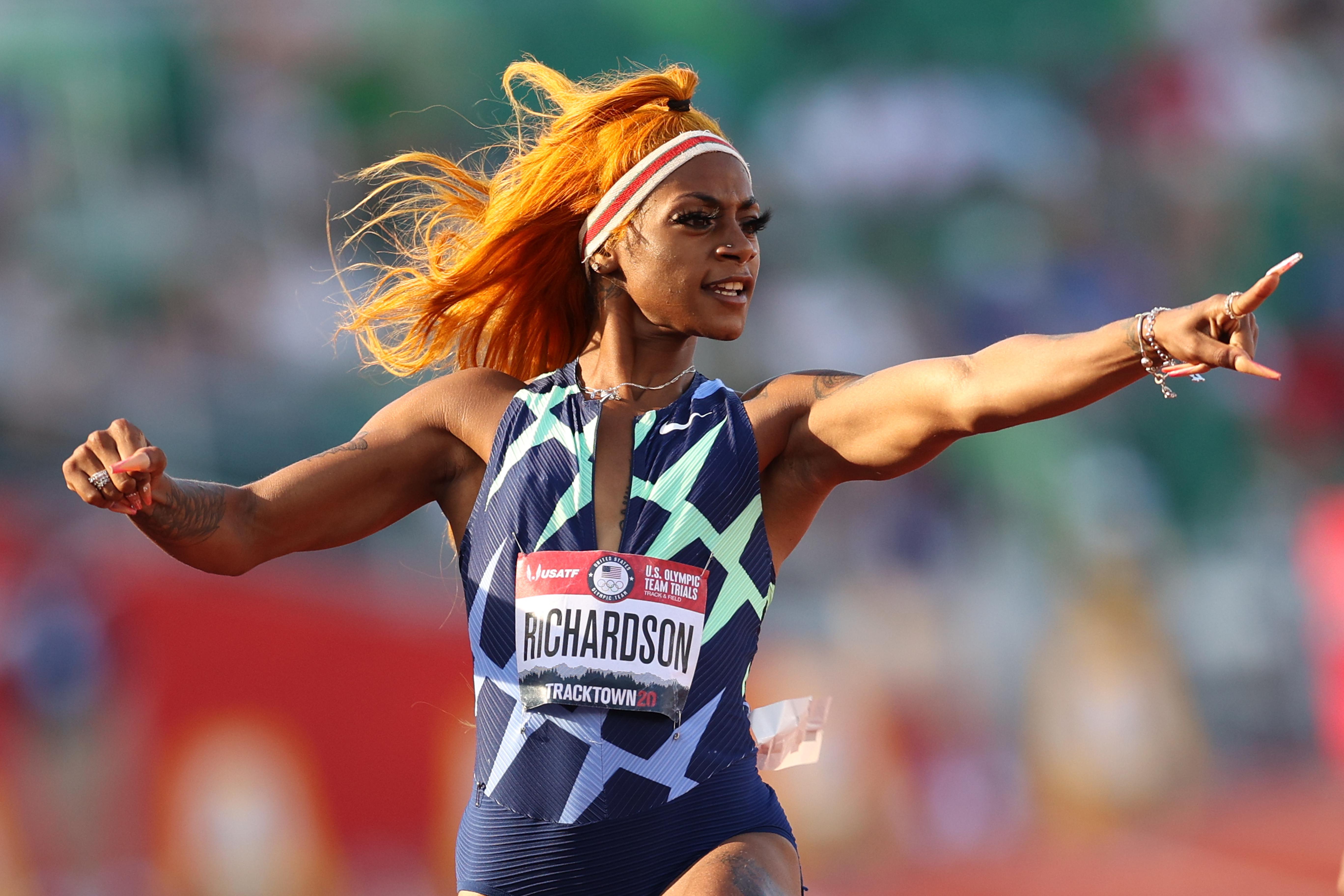 A woman with orange hair points in triumph at the Olympic trials.