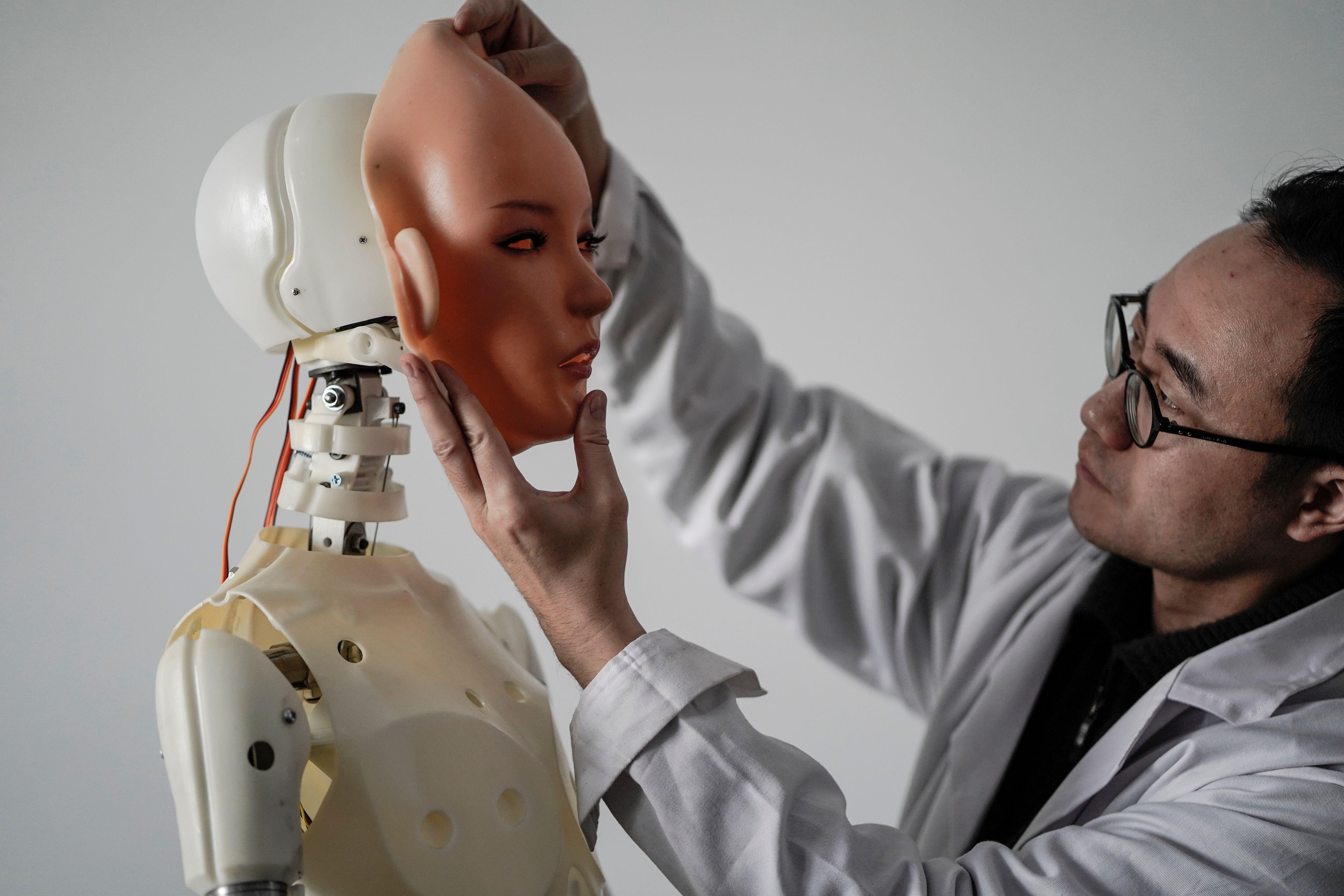An engineer attaches a rubber face to a not-very-convincing-looking sex robot.