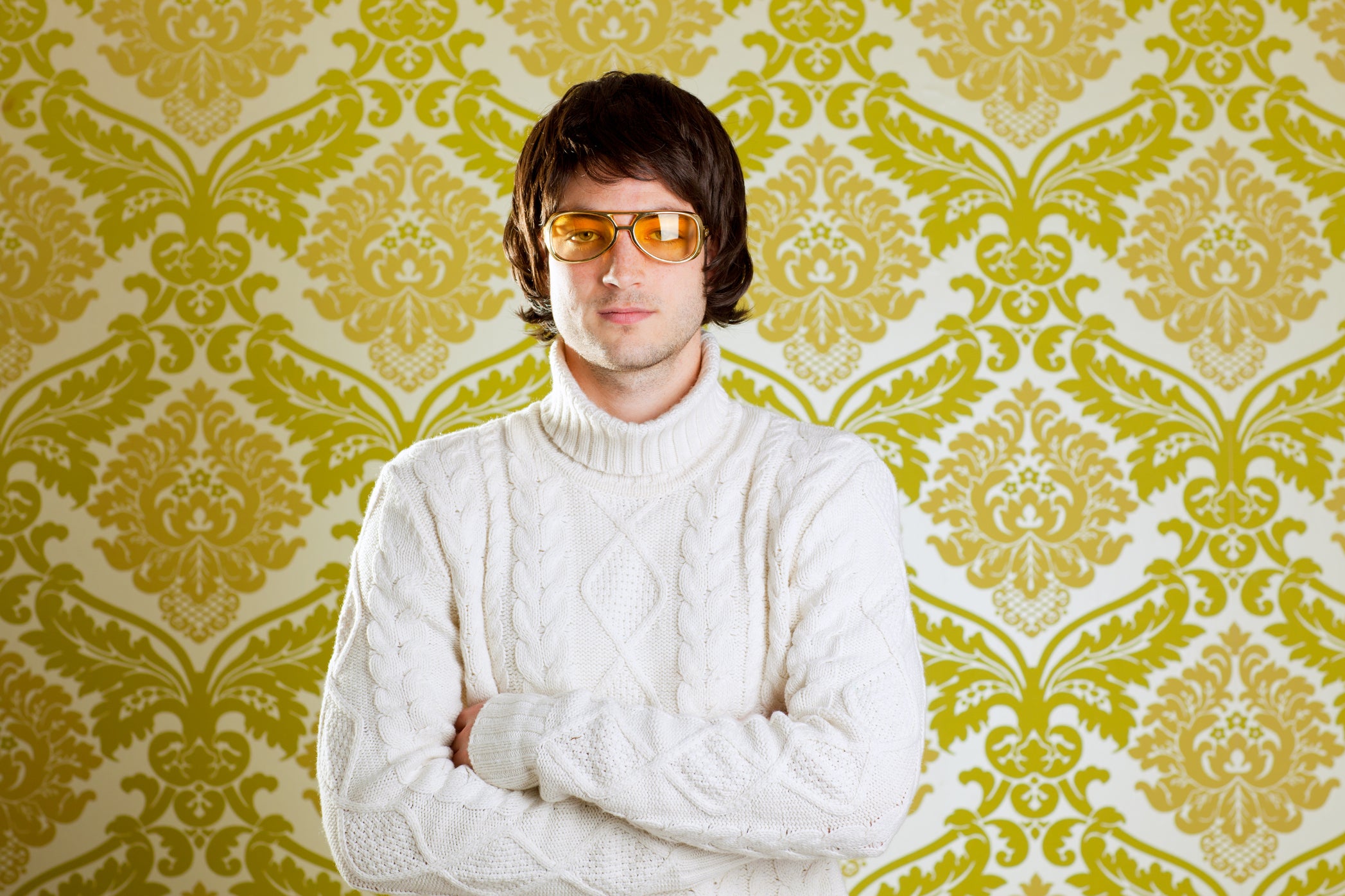 A man in a white sweater in '70s-style aviator glasses.