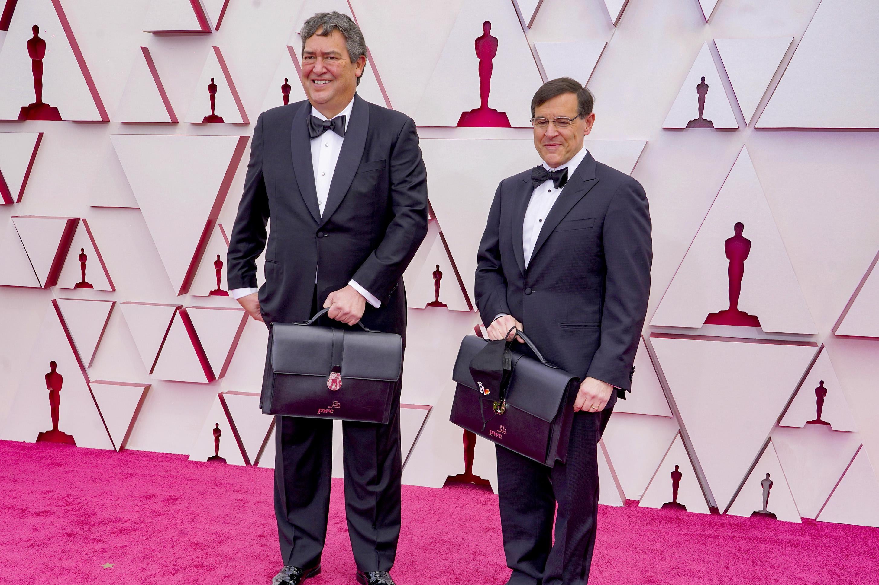 Two PricewaterhouseCoopers employees on the Academy Awards red carpet, holding briefcases with the winners. 