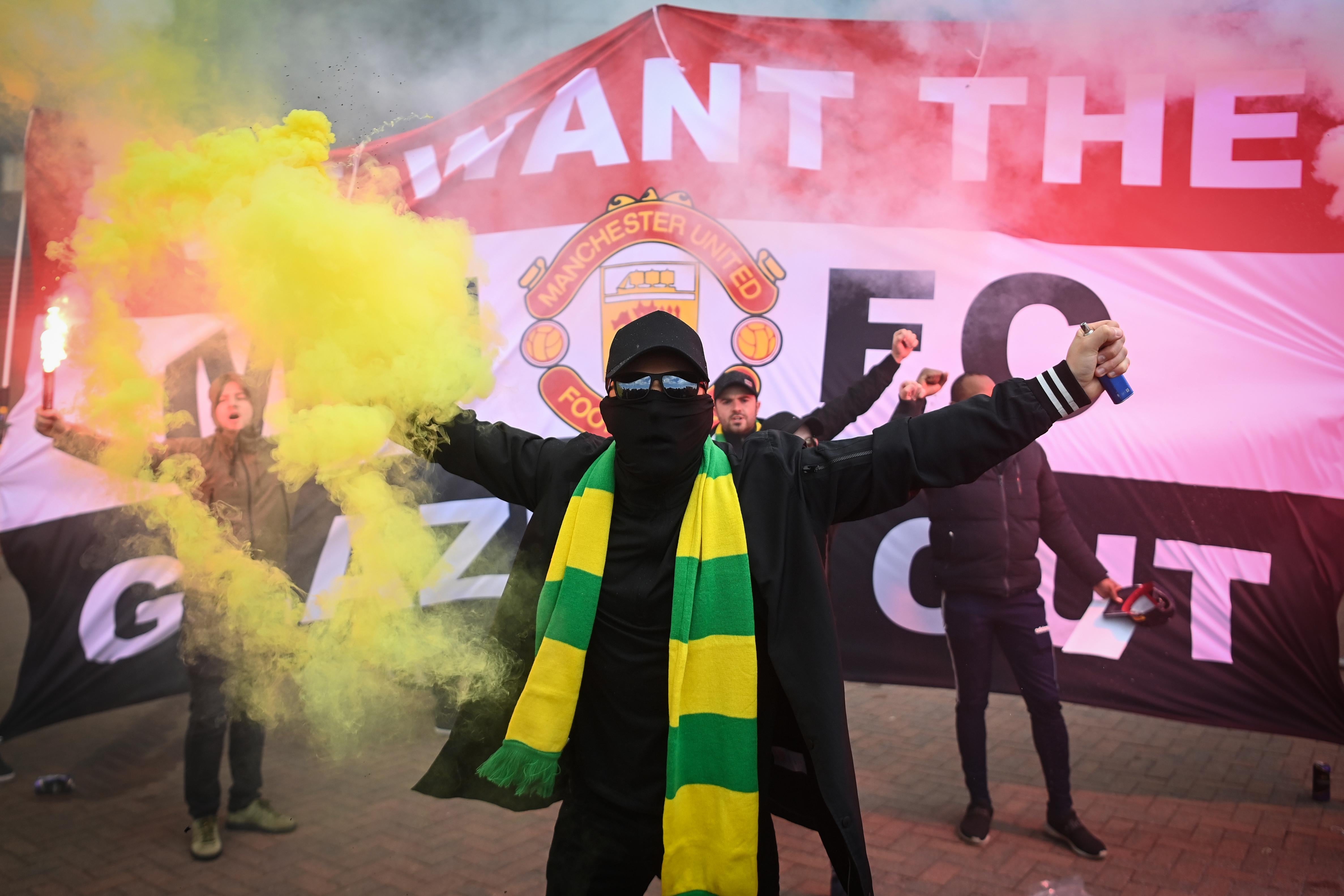 A Manchester United fan holds a flare in front of an anti-Glazer banner.