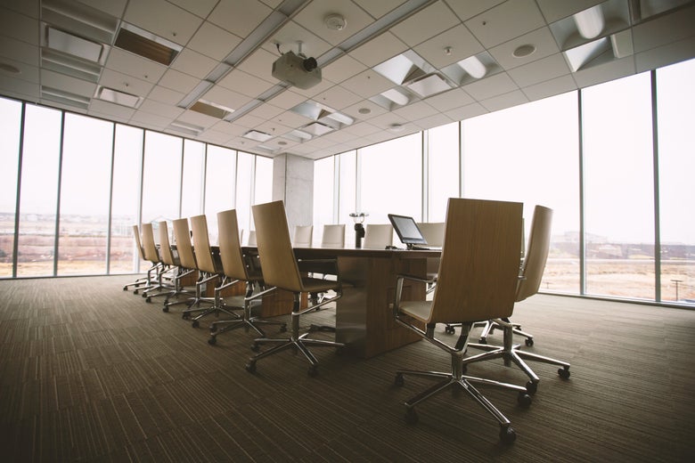 A long, empty conference room table in a corner room with floor-to-ceiling windows.