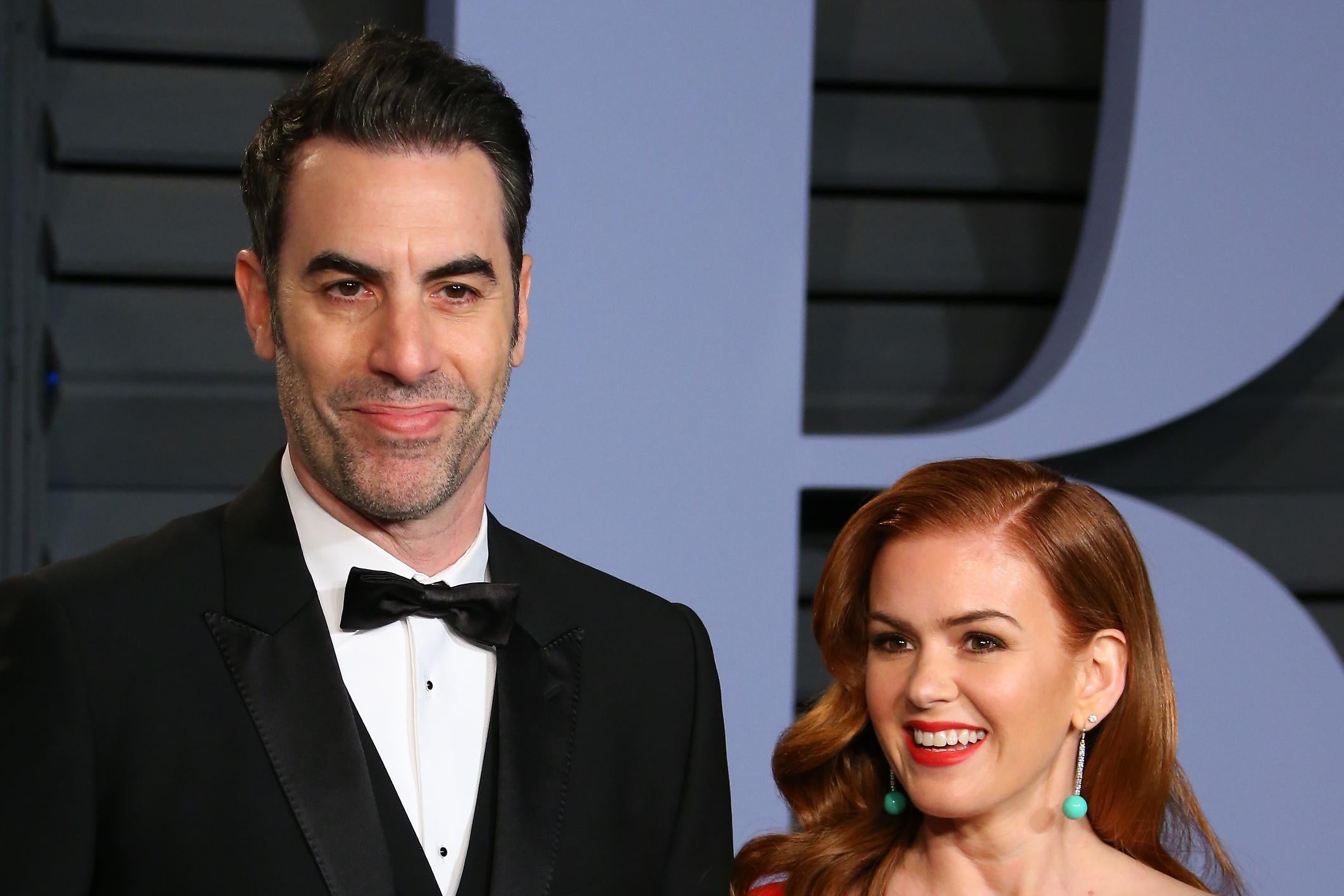Sacha Baron Cohen and Isla Fisher on a red carpet. He is a head taller than she is.