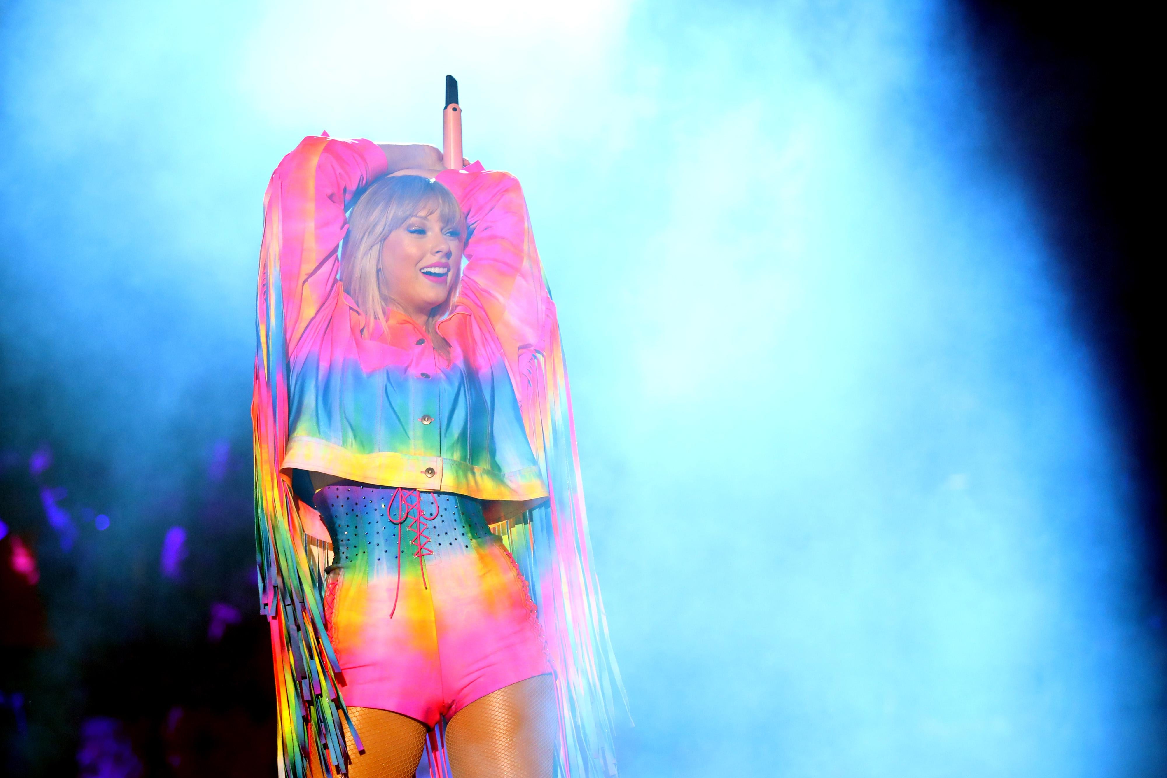 Taylor Swift on stage in a rainbow outfit.