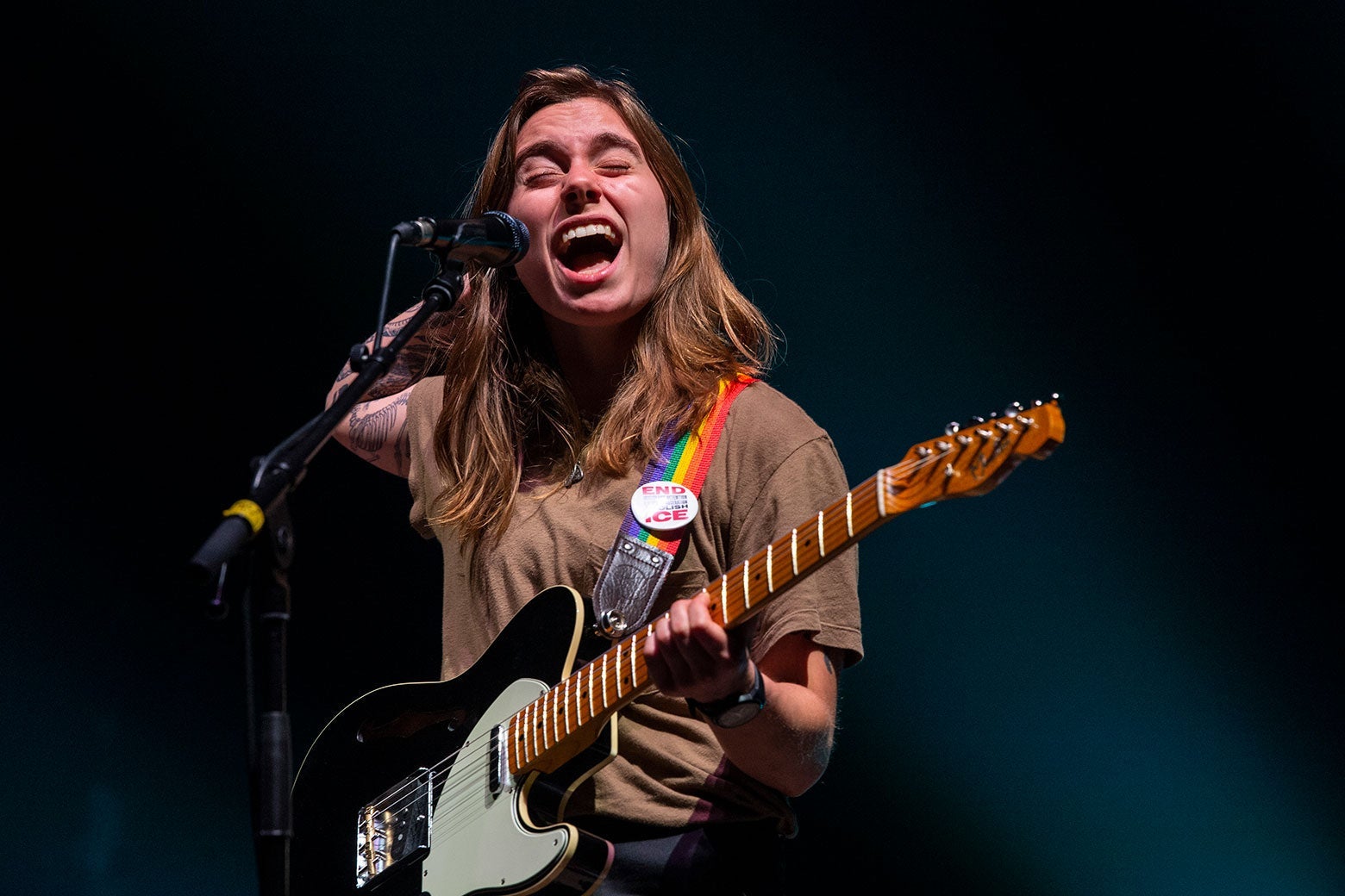 Julien Baker sings into a microphone and plays a guitar with a rainbow strap.