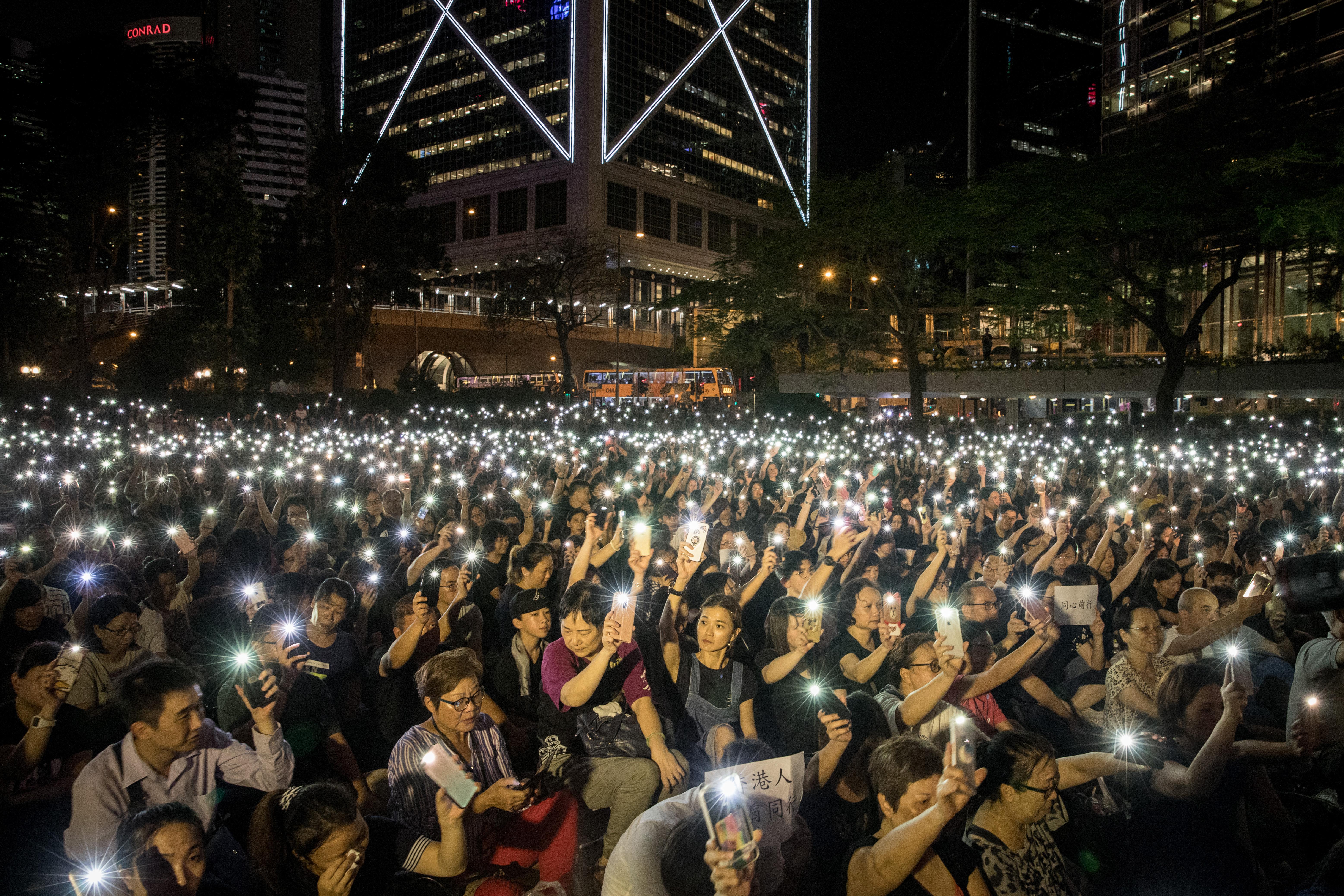 A huge crowd of protesters waving their mobile phones in the air outside at night.