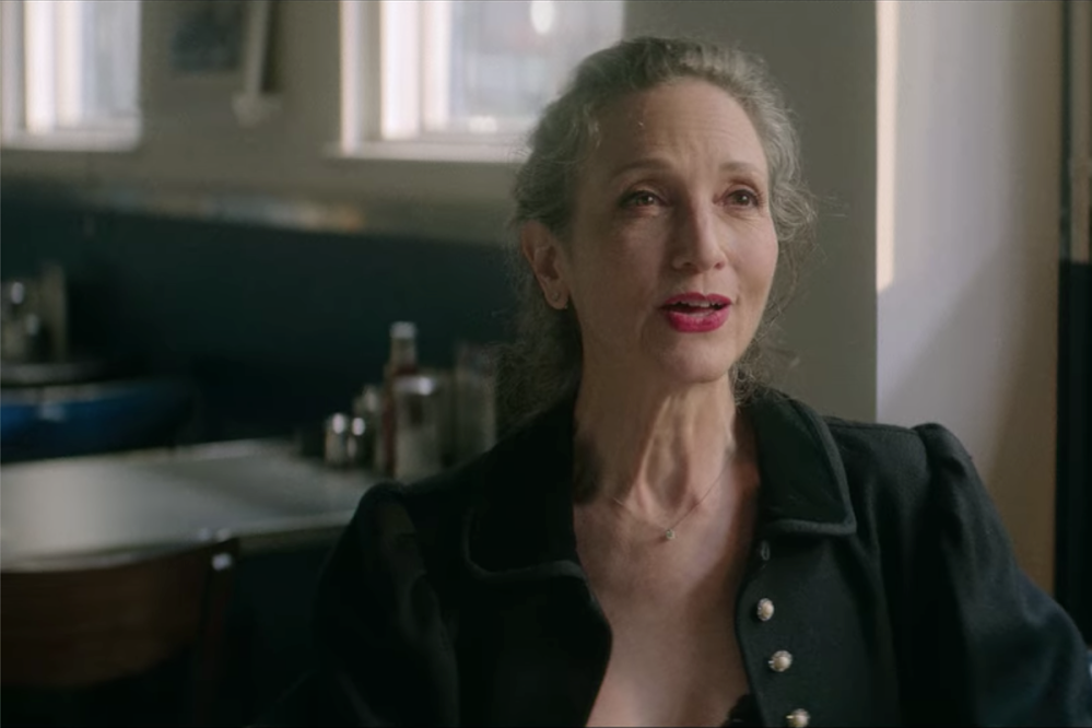 Bebe Neuwirth sits at a diner table singing.