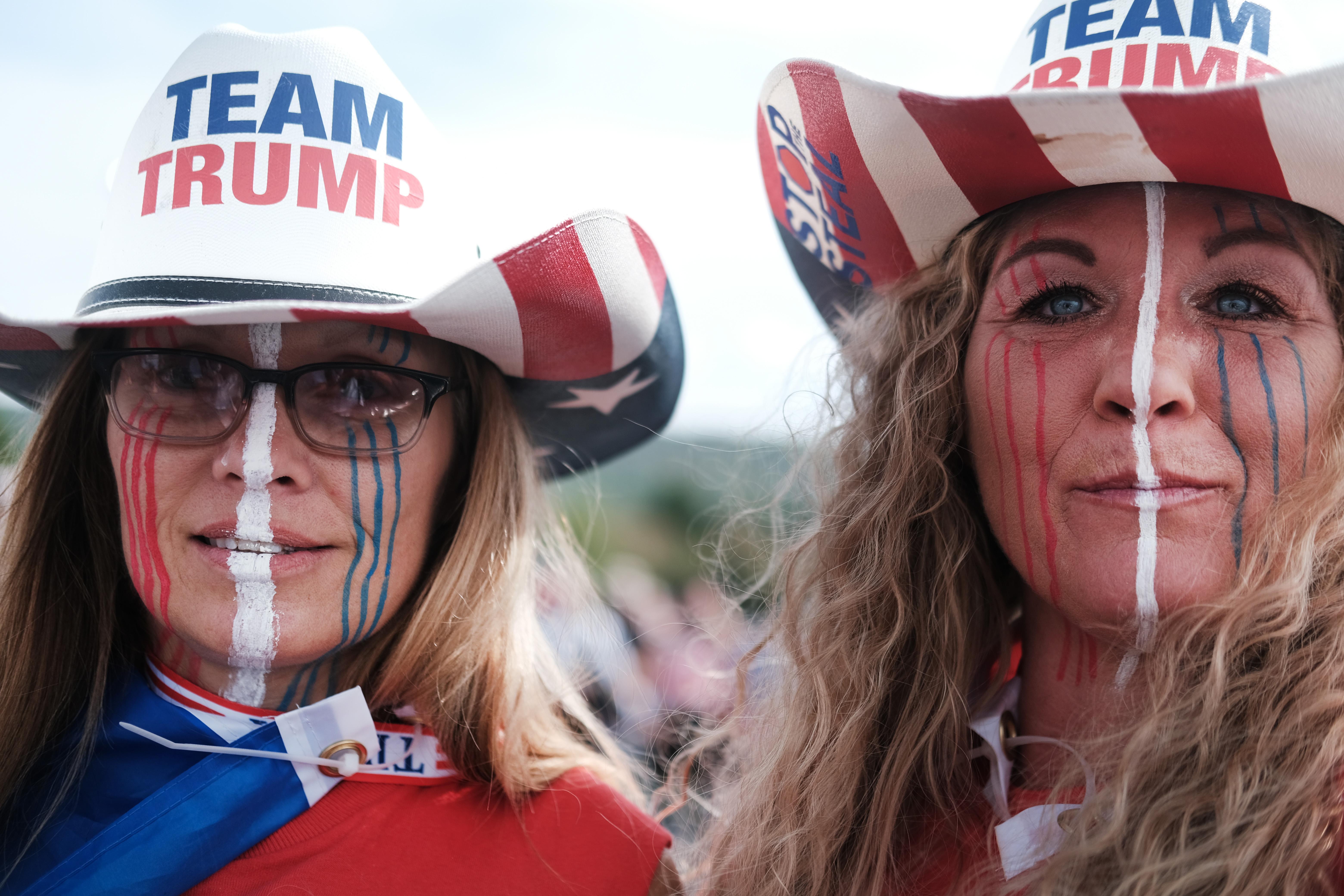 Two women in face paint wearing "Team Trump" hats.