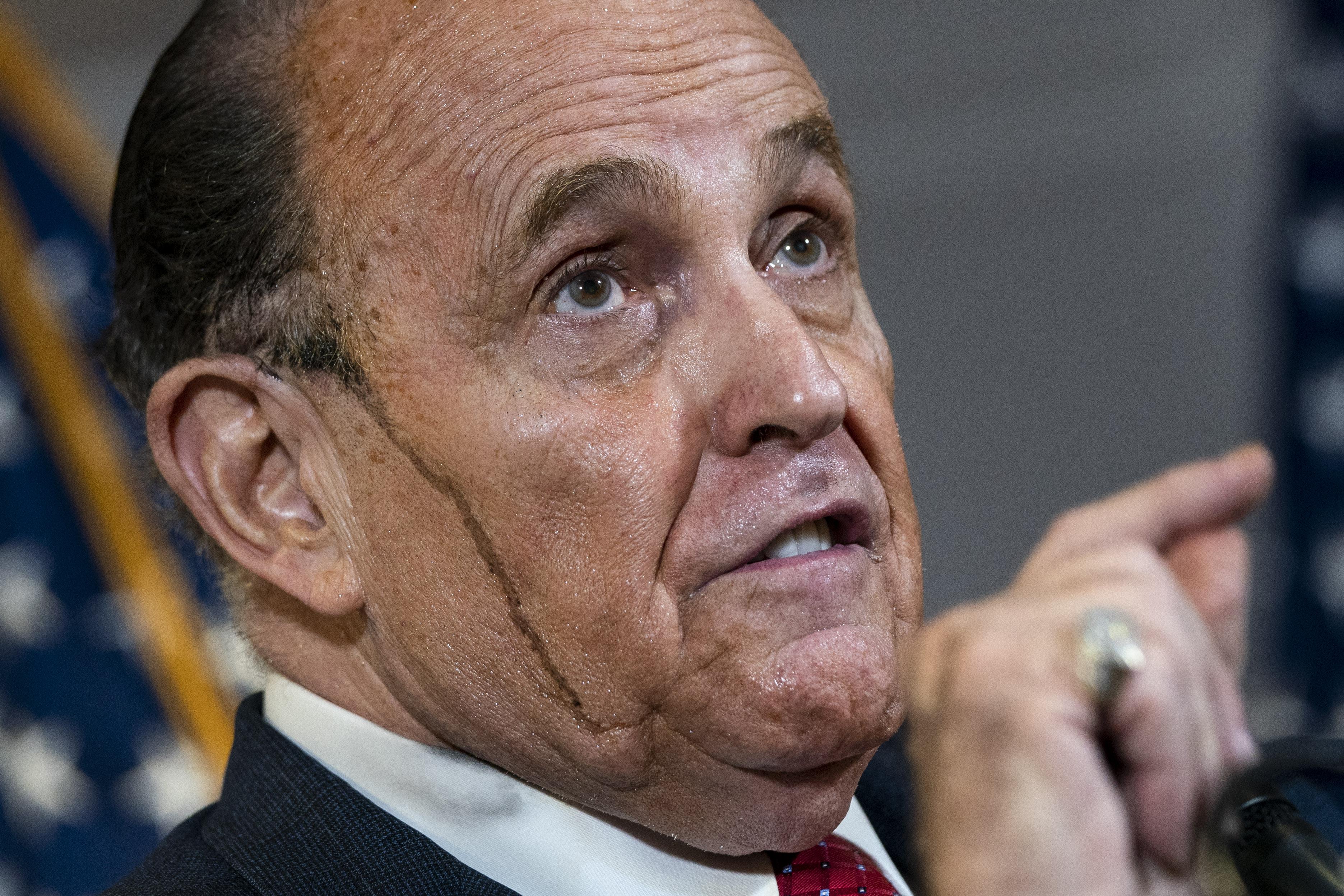 Hair coloring appears to drip down the side of Rudy Giuliani's face as he speaks and points during the press conference