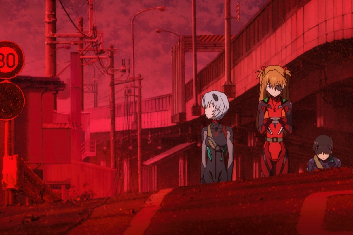 Two women and a man walk in an entirely red landscape, which looks like a post-apocalyptic street. 