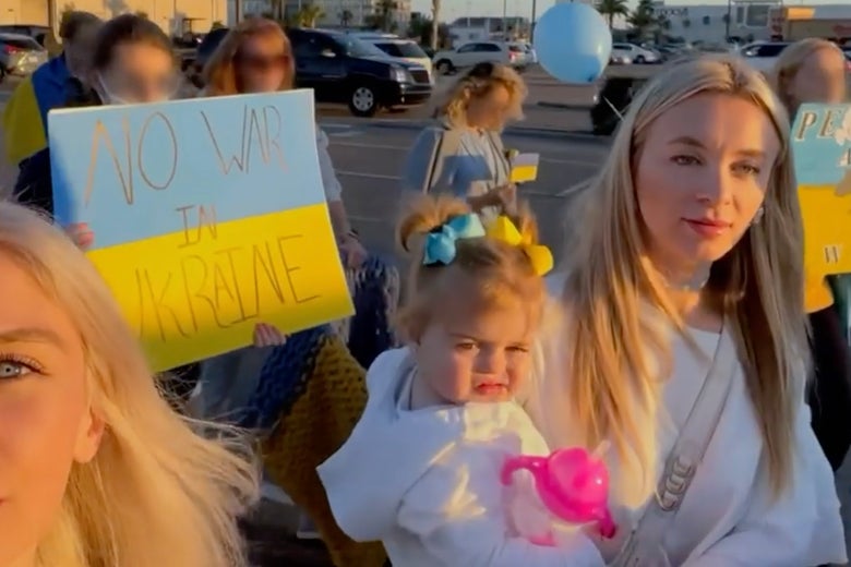 A woman holds a baby among people carrying signs calling for peace in Ukraine