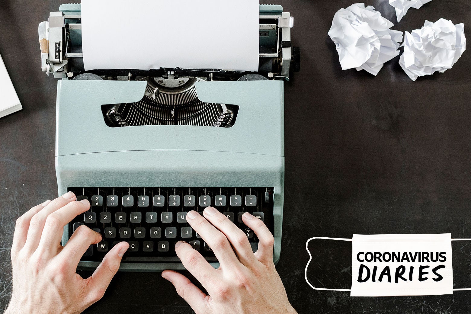 Hands typing on a typewriter next to balled-up papers and a surgical mask that says "Coronavirus Diaries"