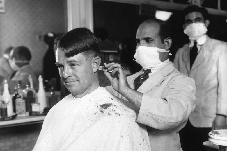 A barber wearing a cloth mask cuts a man's hair
