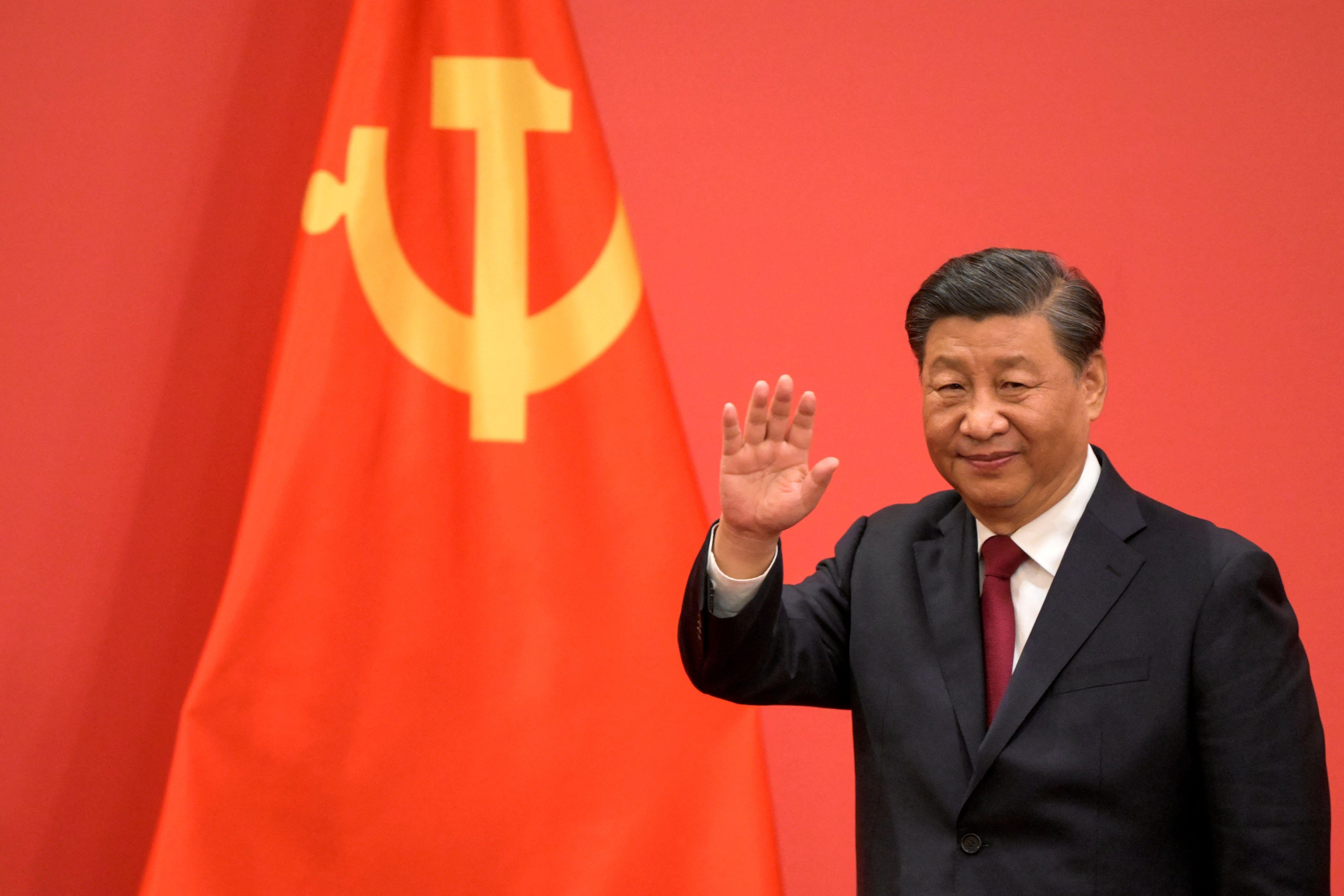 Xi Jinping waves in front of Chinese Communist Party flag.