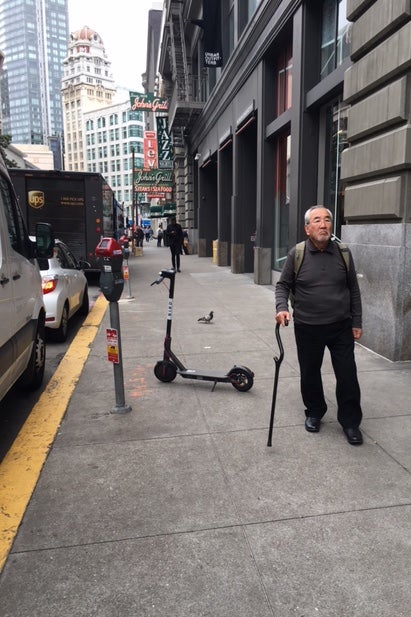 An older man dodges a scooter downtown.