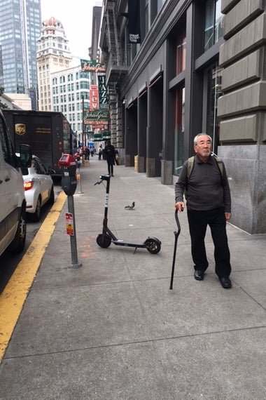 An older man dodges a scooter downtown.