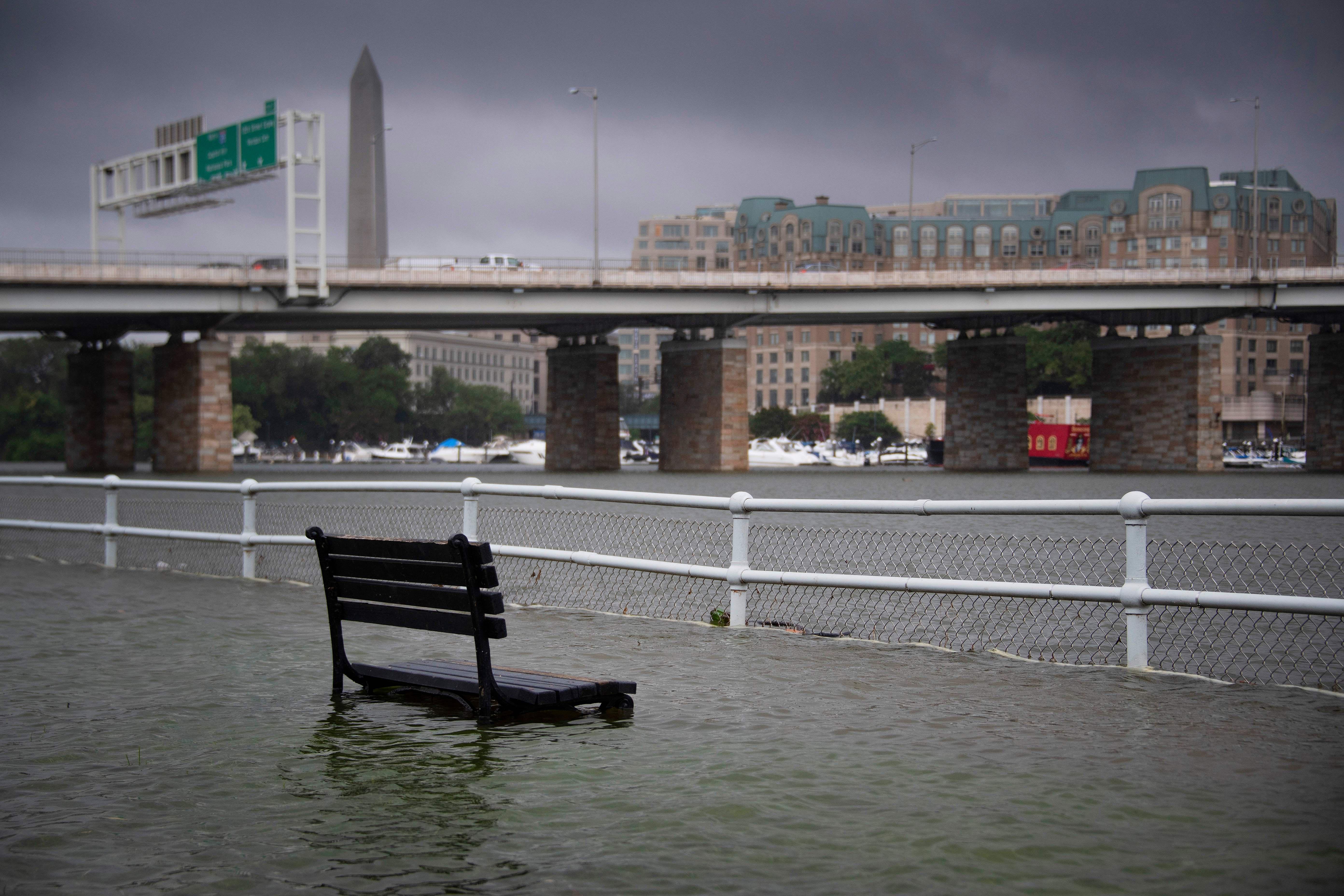 Waters nearly cover a park bench along the river near a bridge in Washington