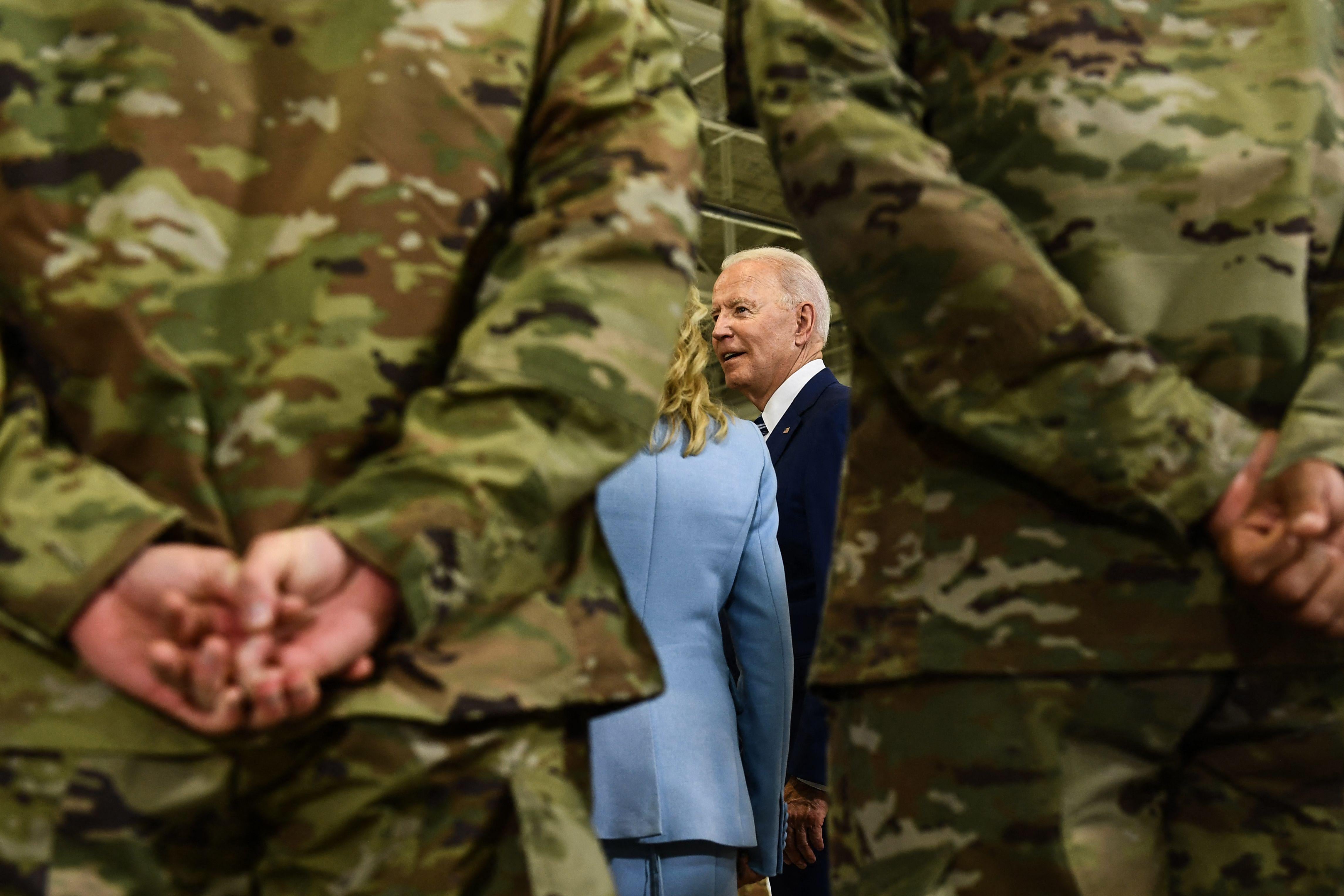 Low angle shot of Biden seen between two military personnel in uniform standing with hands clasped behind their backs