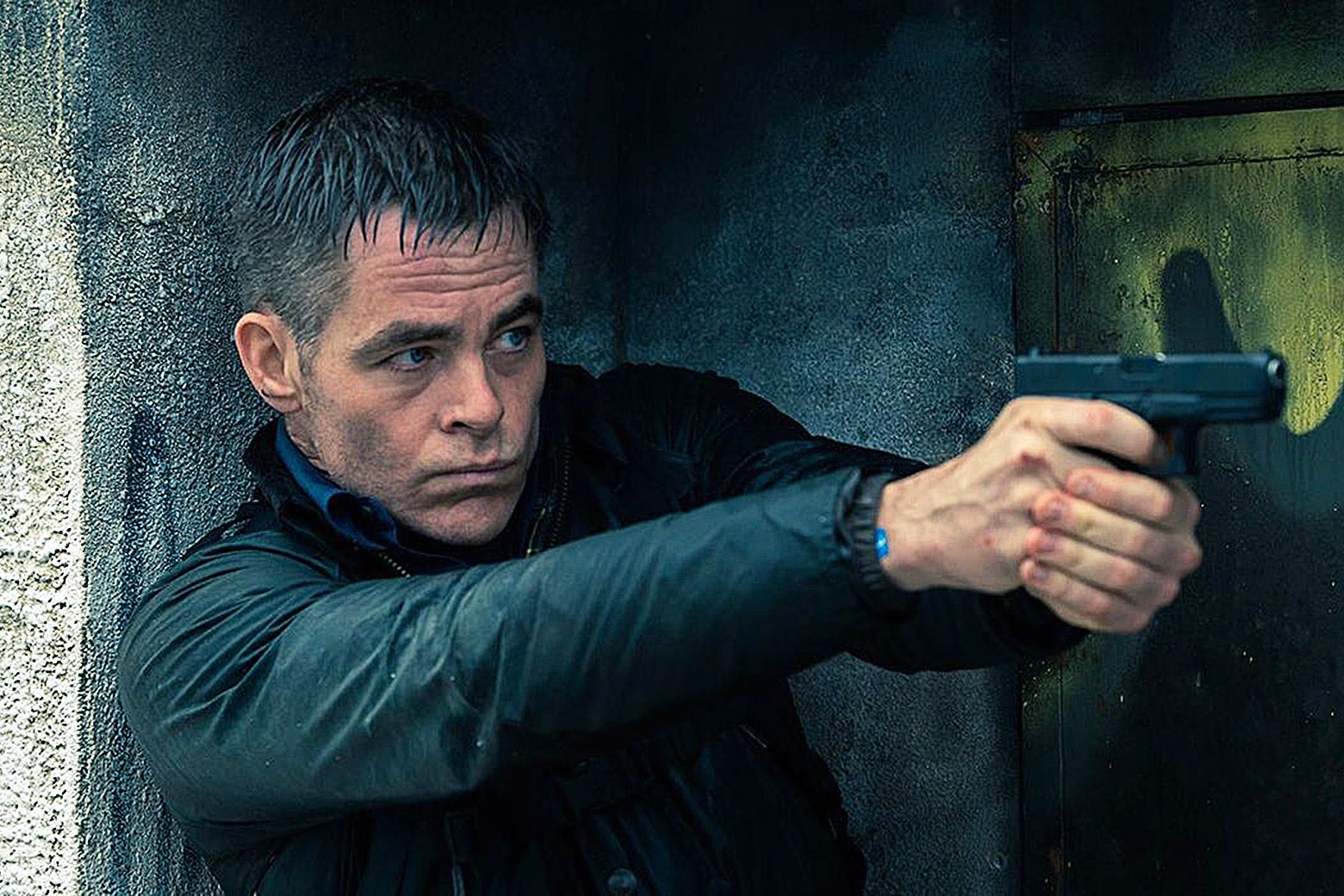 Chris Pine holds a handgun as he stands against a wall.